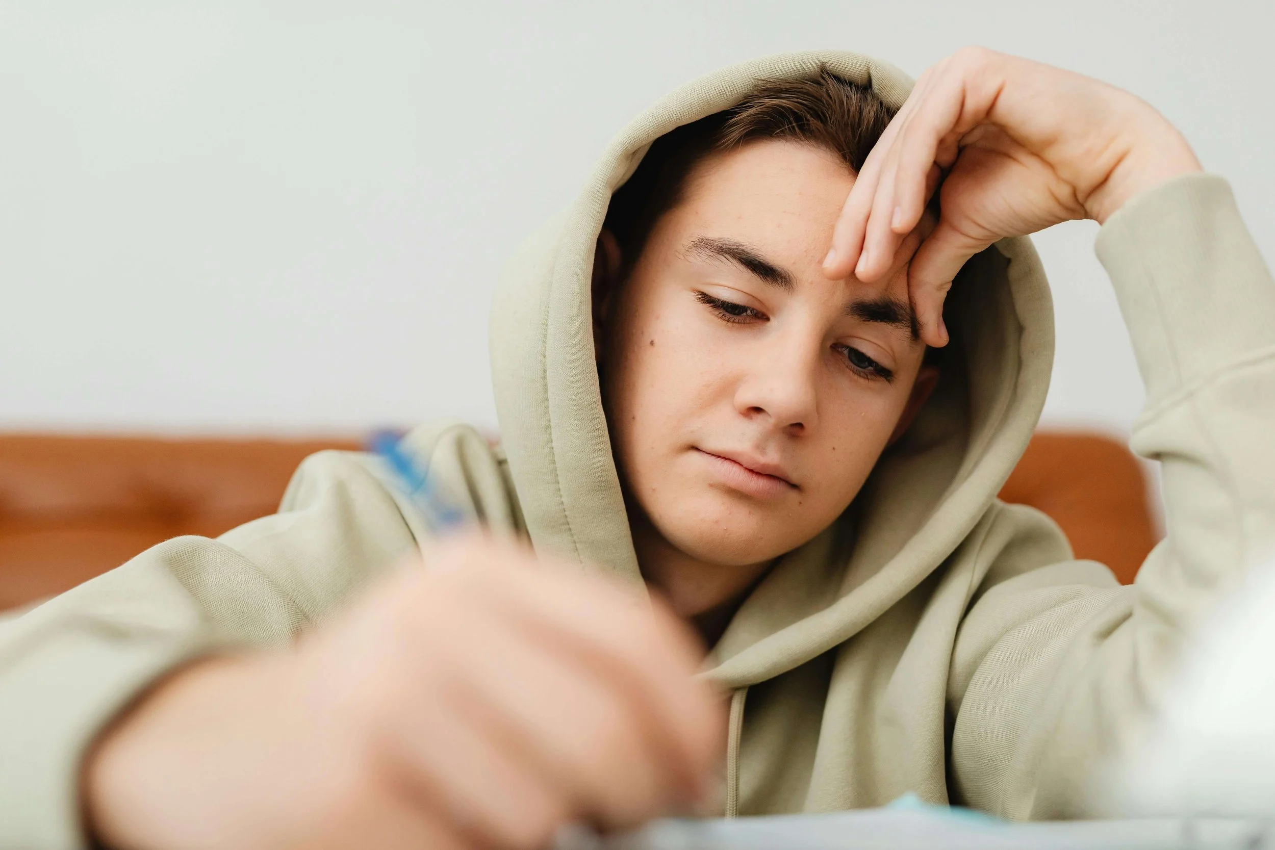 Teenage boy in green hoodie holding a pencil with a hand on forehead appearing stressed. Don't wait for struggles to deepen, explore support options with teen counseling in Tampa, FL.