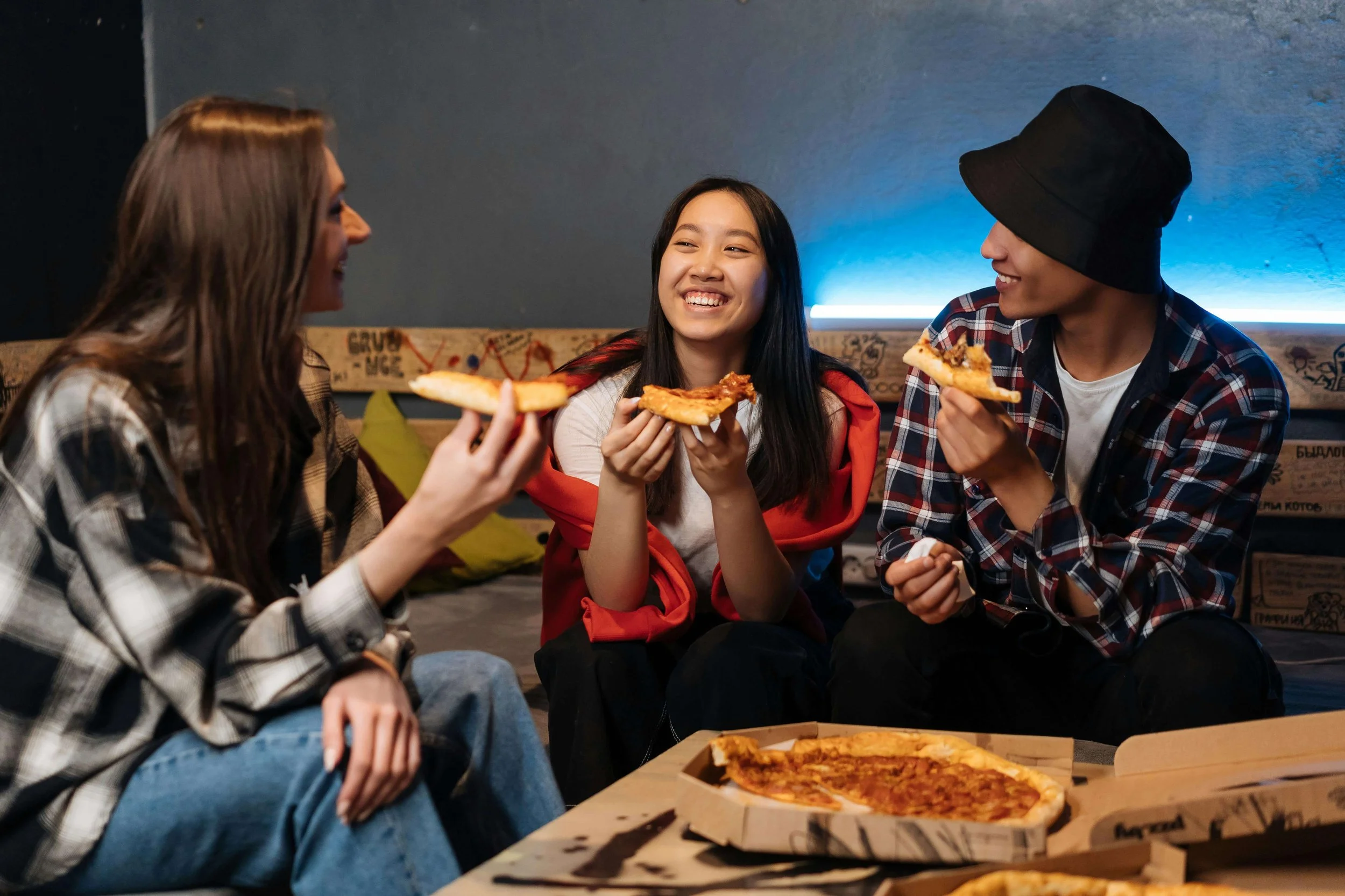 Three teenagers laughing and eating pizza together in casual setting. Help your teen navigate anxiety, pressure, and social struggles with teen counseling in Tampa, FL.