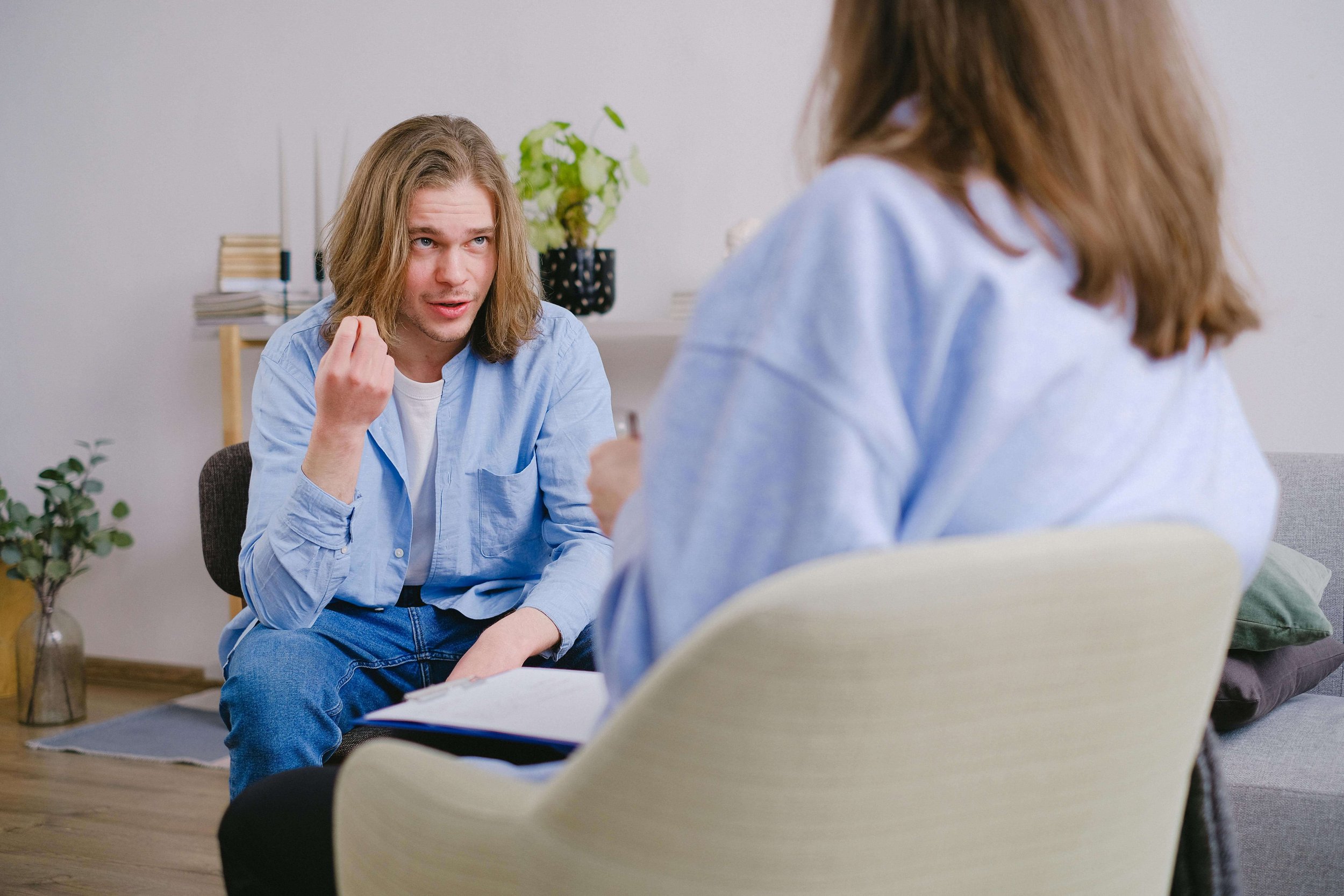 A man with long blonde hair speaking to a therapist in a therapy office setting. Taking that first step and actually talking to someone is where the shift begins and anxiety therapy in Tampa, FL is here when you are ready to start.