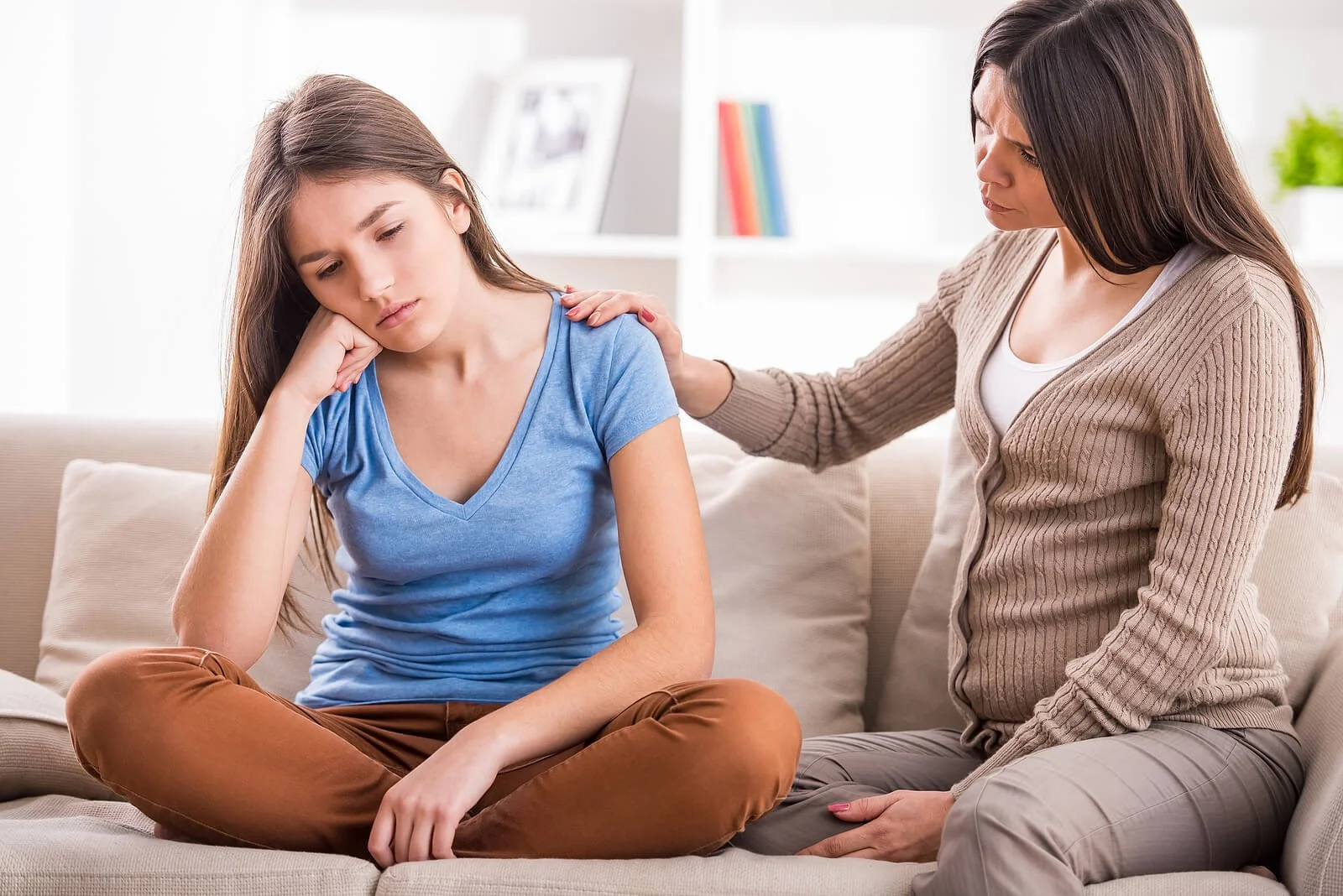 A worried mother gently comforts her upset teenage daughter on the couch, symbolizing the kind of support available through teen counseling near me with a teen counselor in tampa, fl