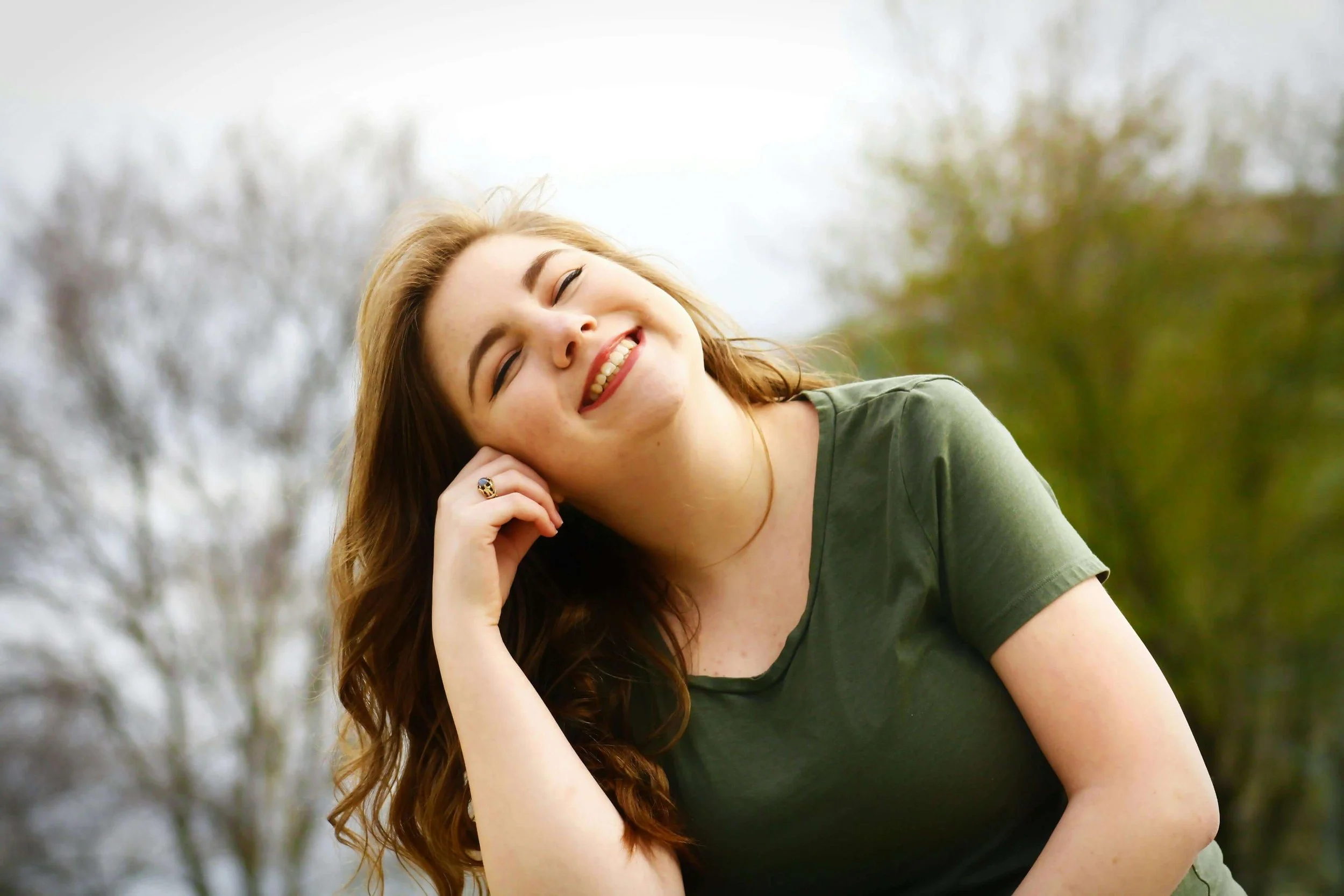 Smiling woman in green shirt with hand in hair outdoors on bright day. Experience complete trauma recovery—body and spirit—with Christian counseling in Tampa, FL.