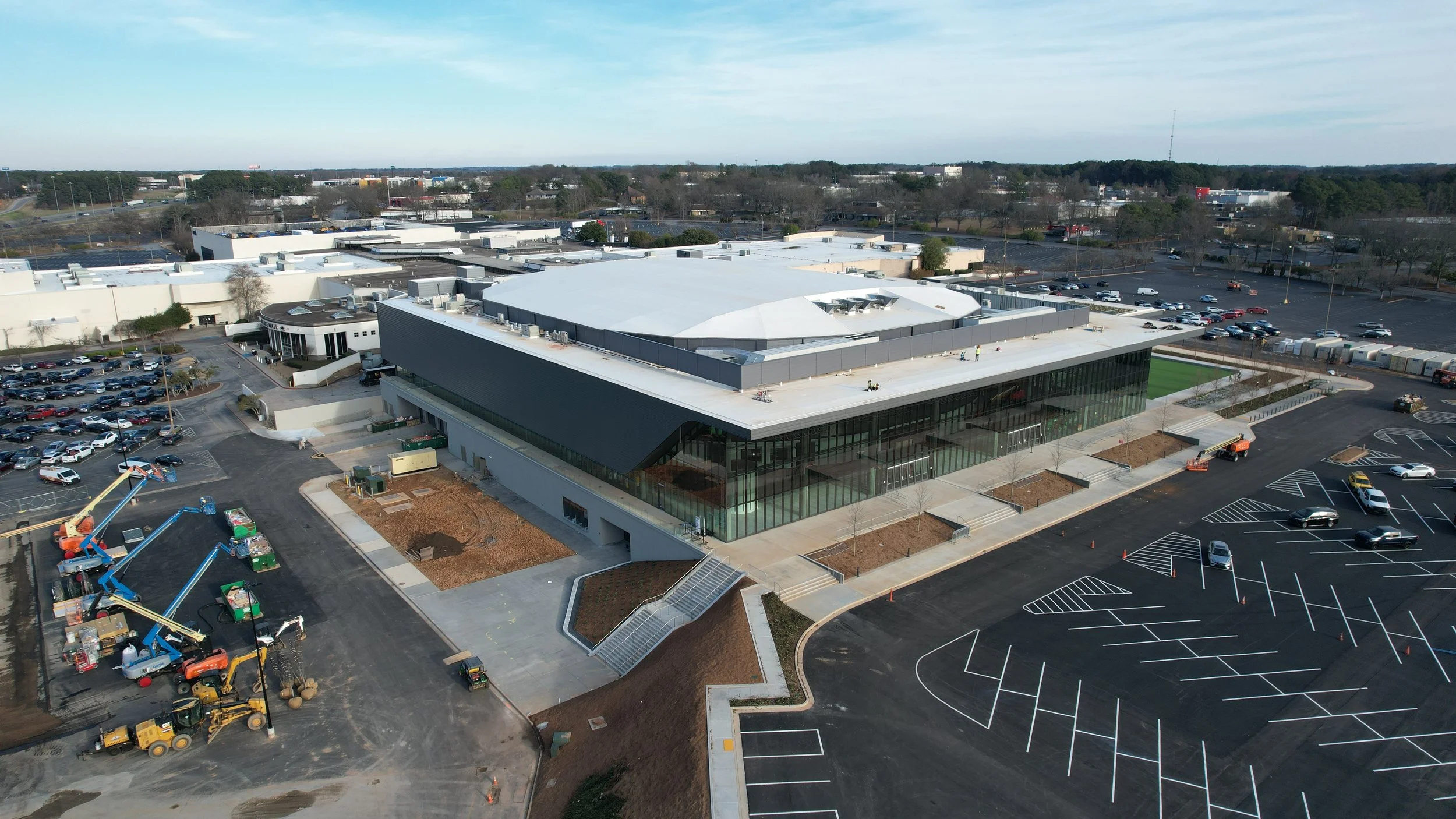 Aerial view of a large modern commercial building under construction with a nearby parking lot and landscaping in progress.