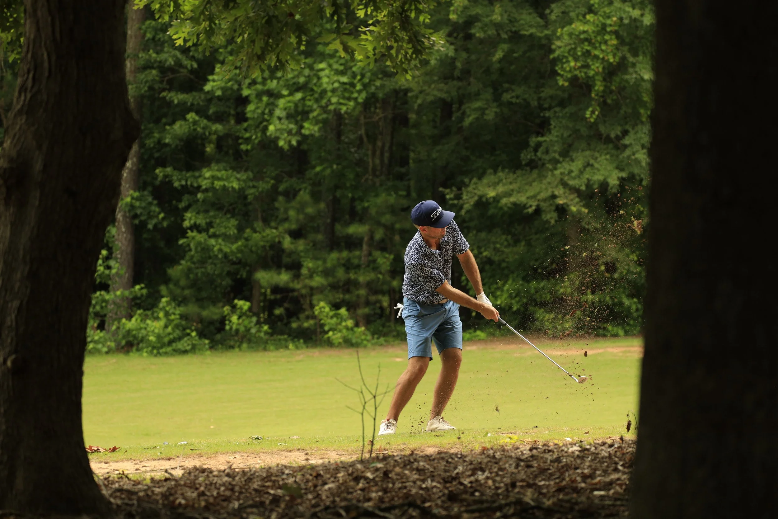 A man playing golf on a course with a wooded background, hitting the ball out of a sand trap.