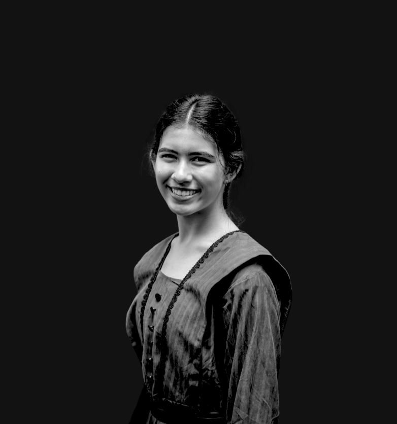 Young woman smiling, wearing a red vintage-style dress with black trim and buttons, standing indoors.