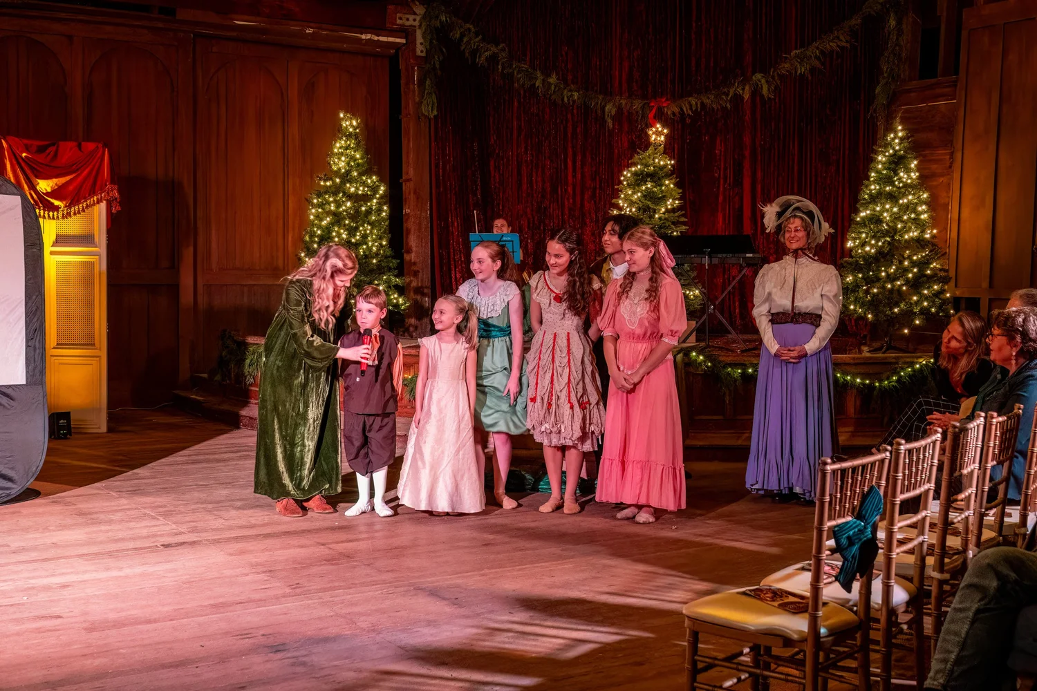 The cast on stage beside Christmas trees.