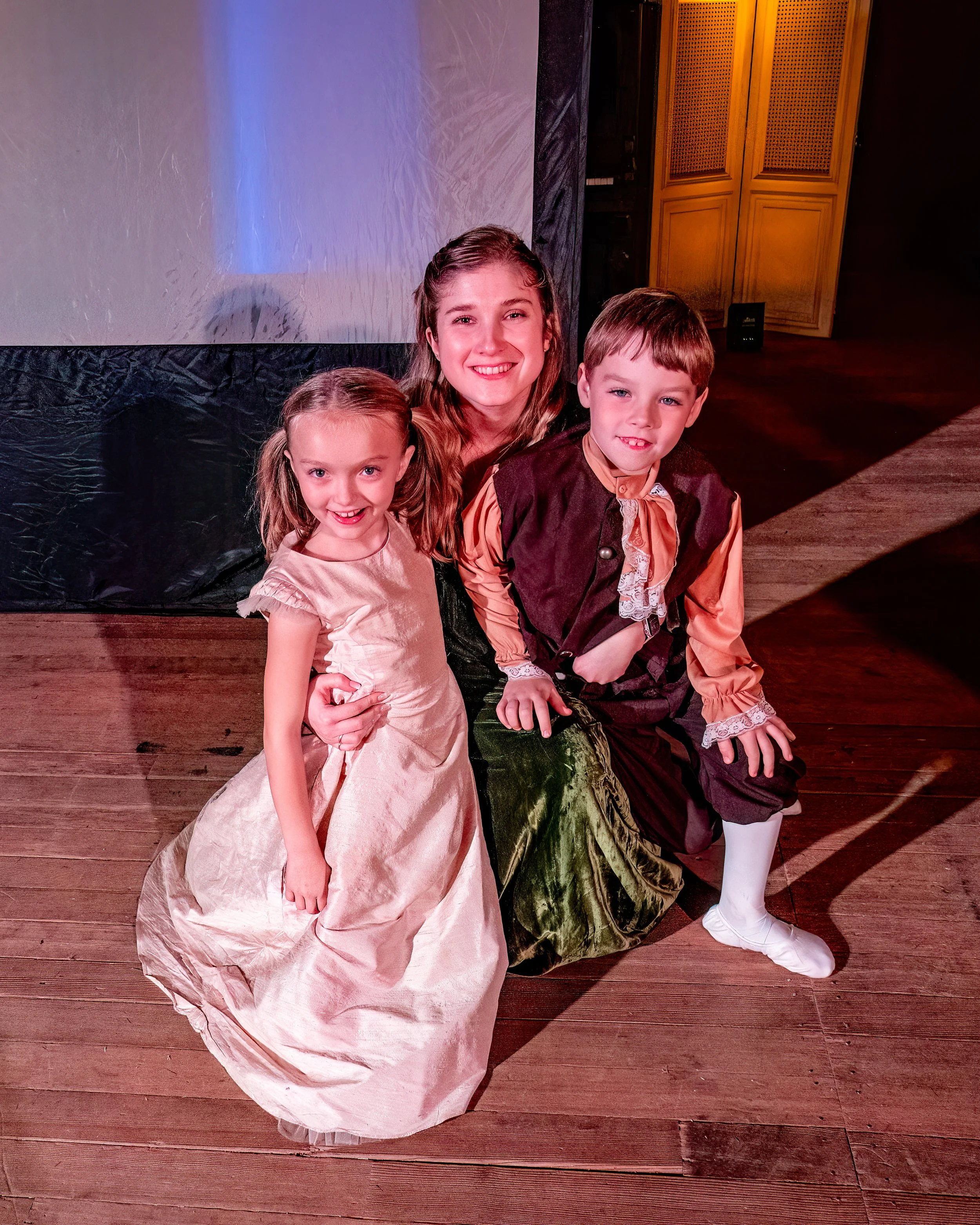 Three children and a woman in costume at a stage event, smiling for the camera.