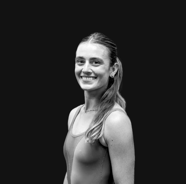 Smiling young woman with long hair in a ponytail, wearing a blue sports top, in an indoor gym or fitness space.