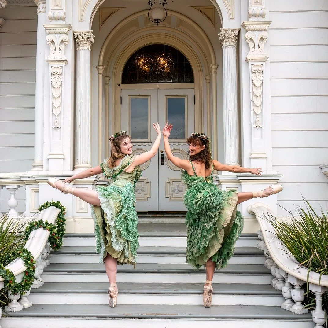 Two women dressed as fairies in green costumes performing ballet on the steps of a white ornate building