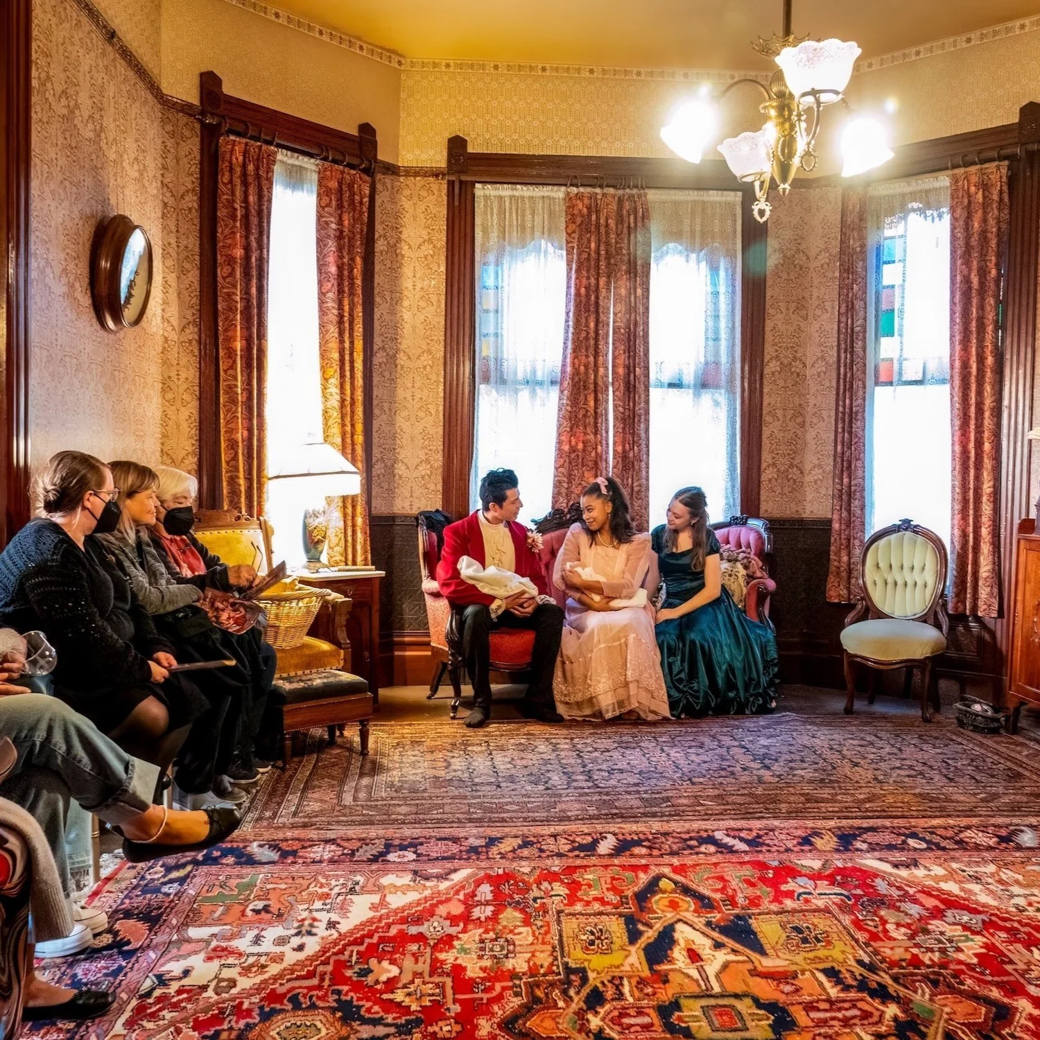 Audience seated in an ornate Victorian living room as costumed dancers perform