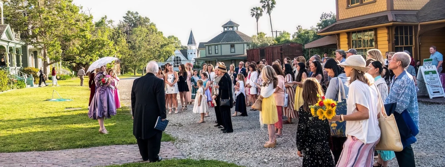 Guests and cast in Victorian attire gathered outdoors at Heritage Square Museum