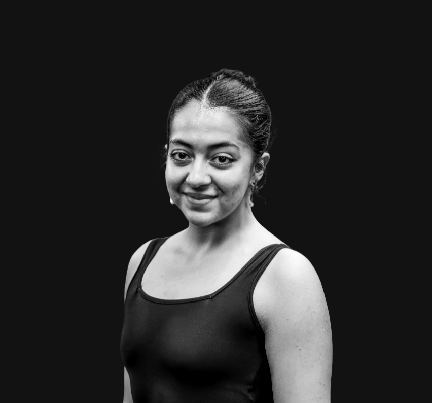 Portrait of a young woman with dark hair tied back, wearing a navy sleeveless top, smiling softly against a plain background.