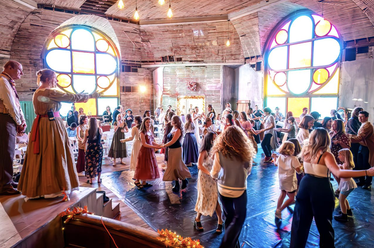 Guests in modern and Victorian attire social dancing together in a hall with two large stained-glass rose windows