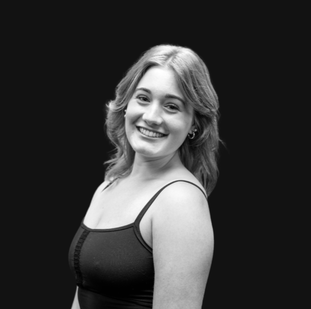 A young woman with light brown hair styled in loose waves, smiling while facing slightly to the right, wearing a pink top with lace details.