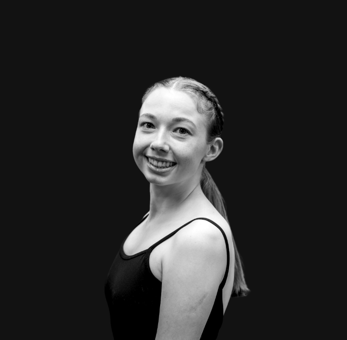 A young woman with light skin, long reddish-brown hair in a braid, wearing a teal satin dress with puffed sleeves, and a black lace choker, smiling at the camera in an indoor setting.