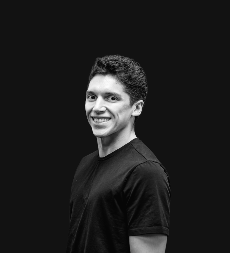 A young man with dark, curly hair wearing a black tuxedo with a bow tie, smiling at the camera.
