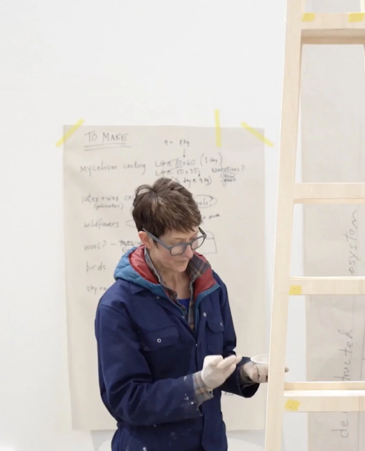 Kelly M O’Brien wearing glasses and gloves, working on a sculpture beside a wooden frame during her PADA residency.