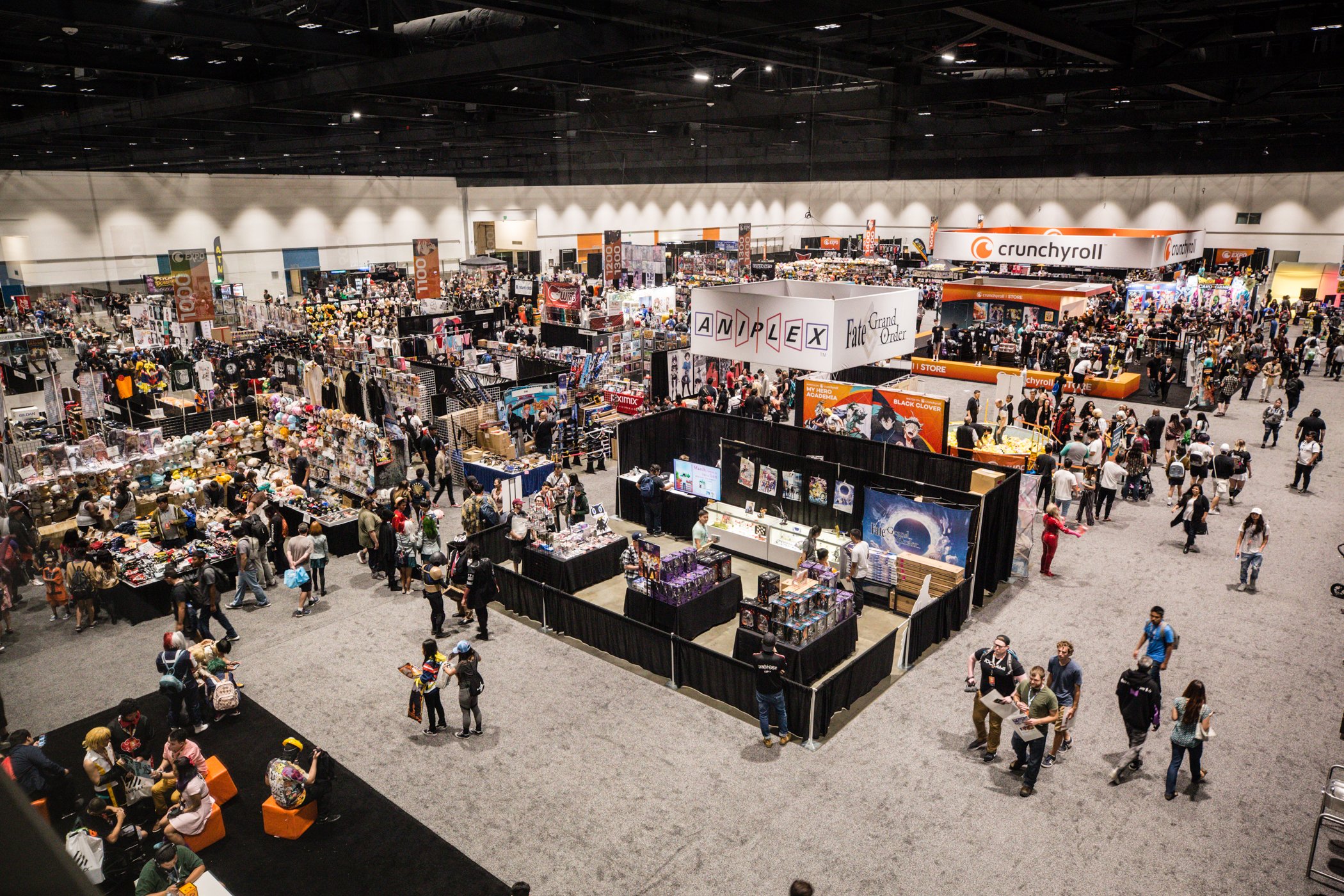 Crowd of people walking around and shopping at a large convention or expo with various booths and displays, including merchandise for anime, comics, and pop culture.