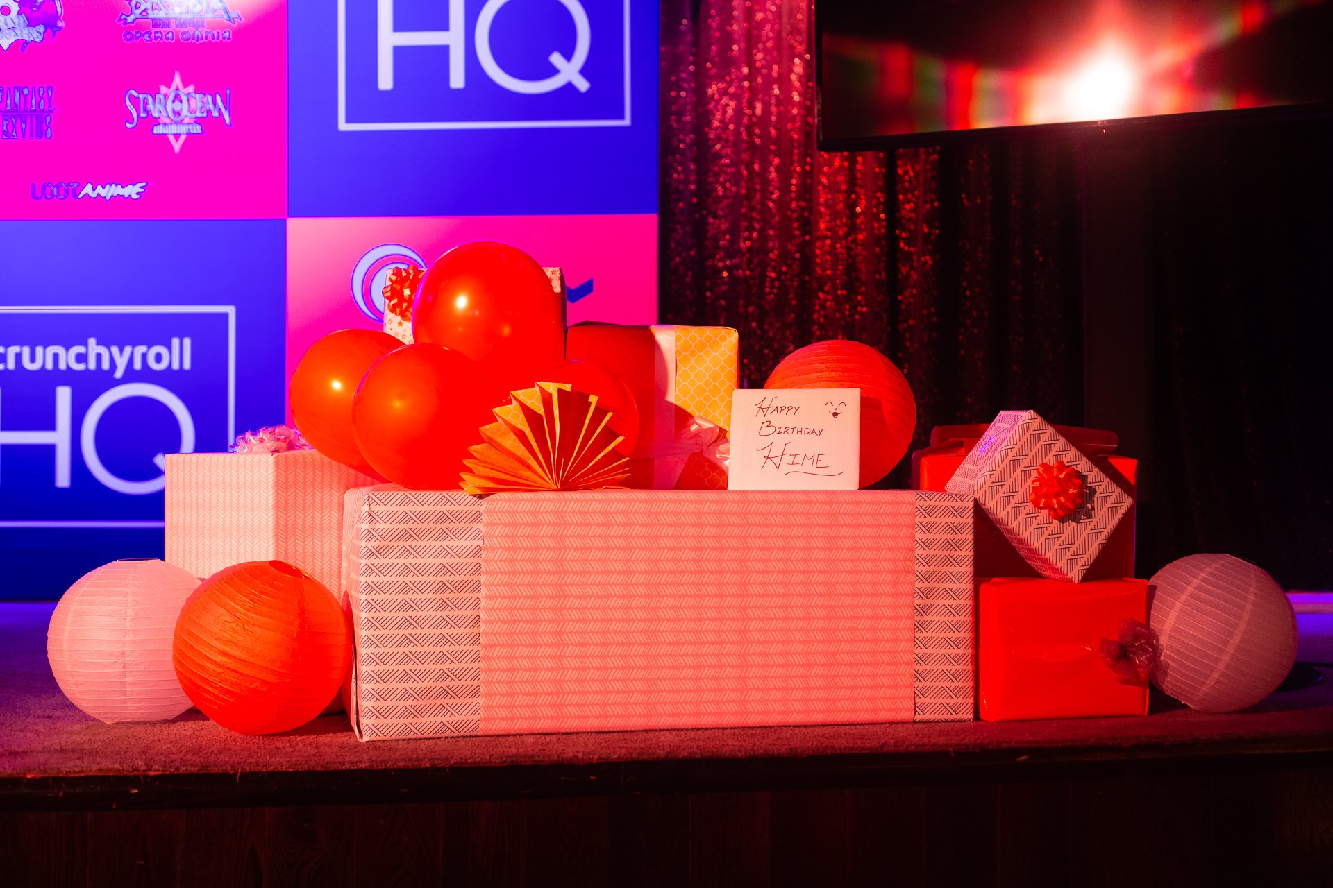 Gift boxes, balloons, and a handwritten birthday note on a decorated stage with a digital screen background.