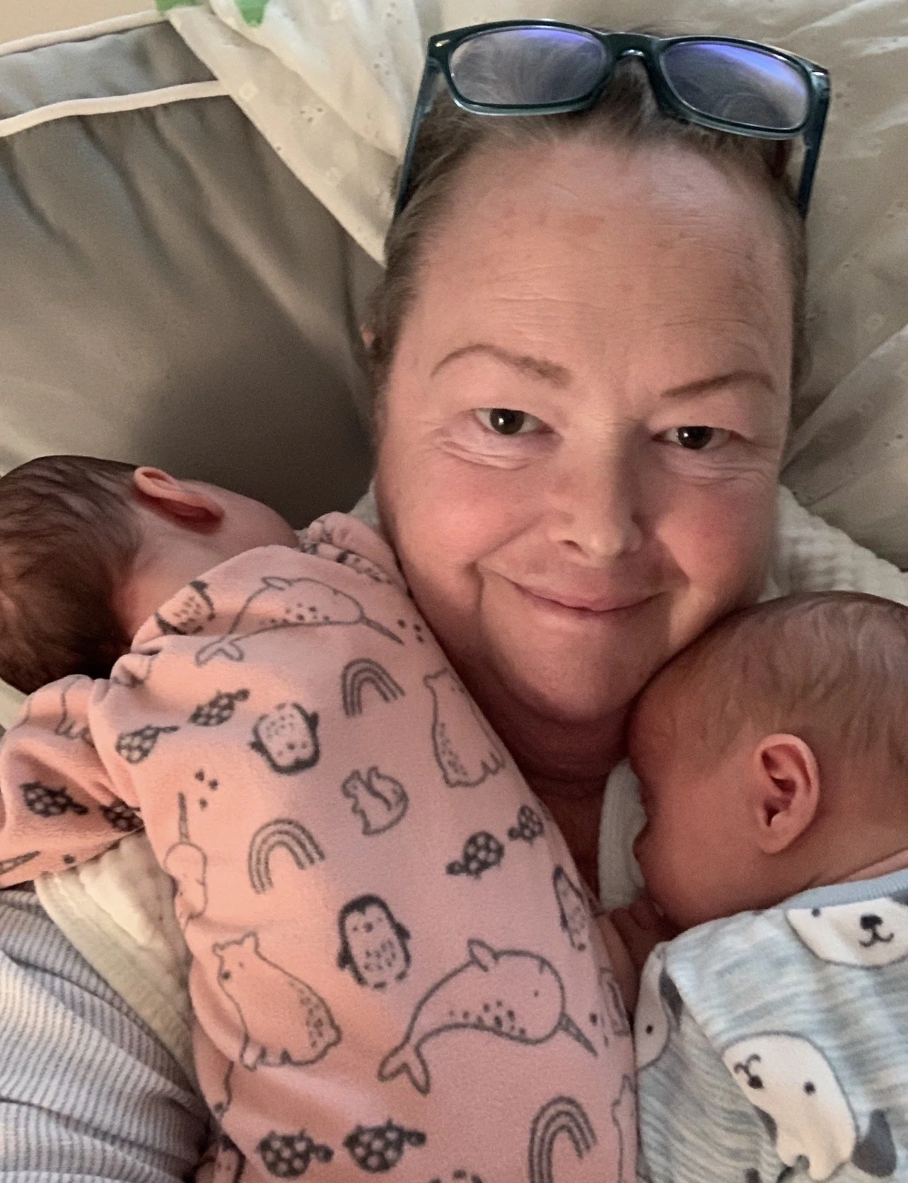 A baby lying on a hospital bed, being held by an adult with their hands gently grasping the baby's legs, with the baby's gaze directed upward.