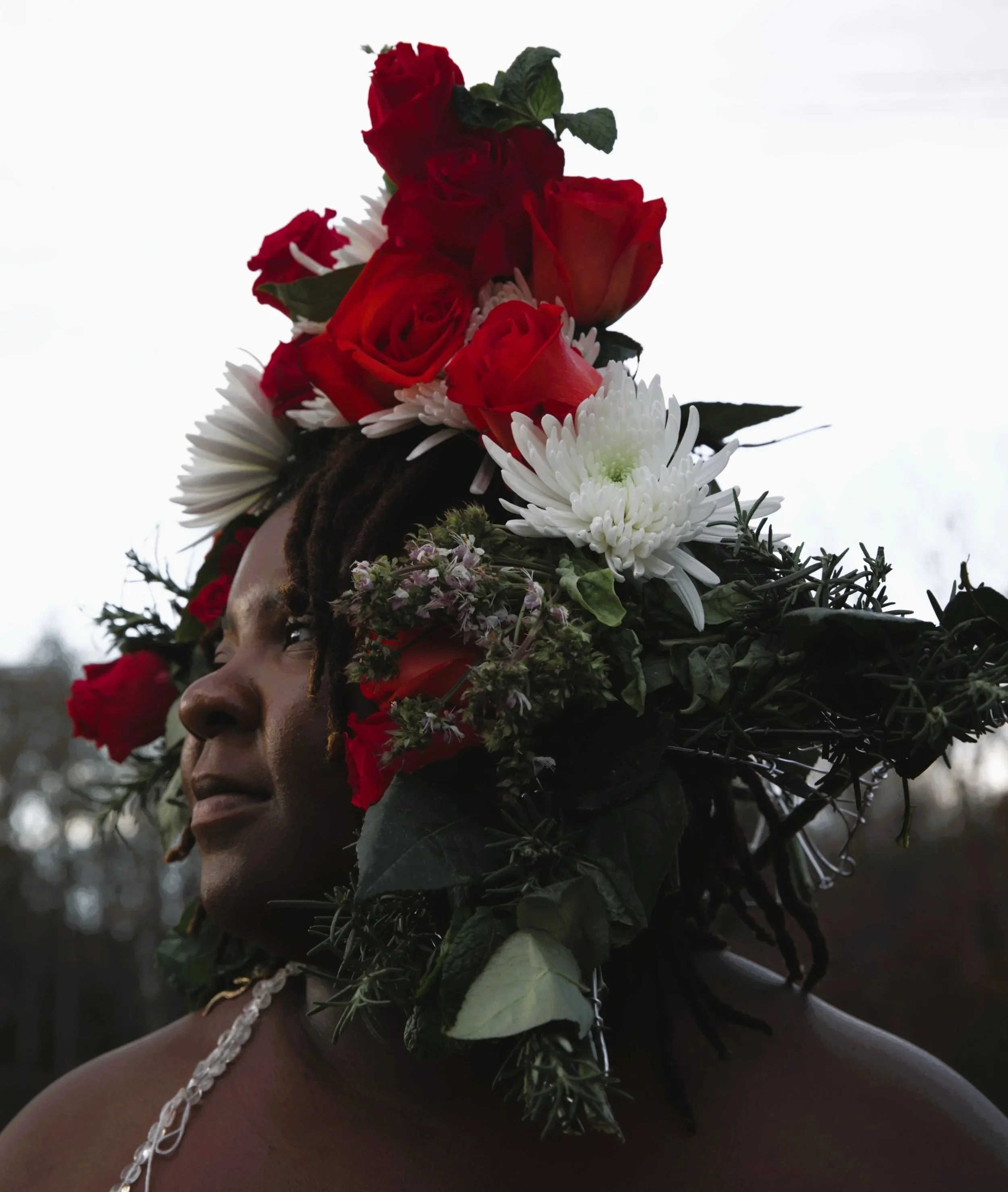 A person with dark skin and long hair holding a bouquet of red roses and white daisies against a plain white background.