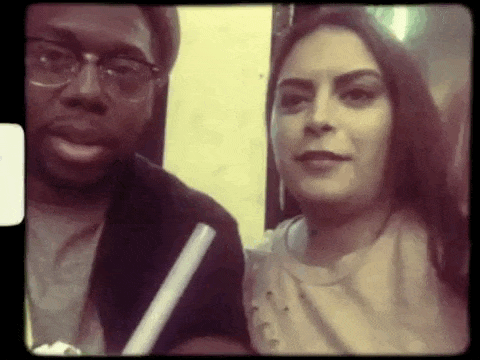 A man and a woman taking a selfie together, both looking at the camera in an indoor setting.