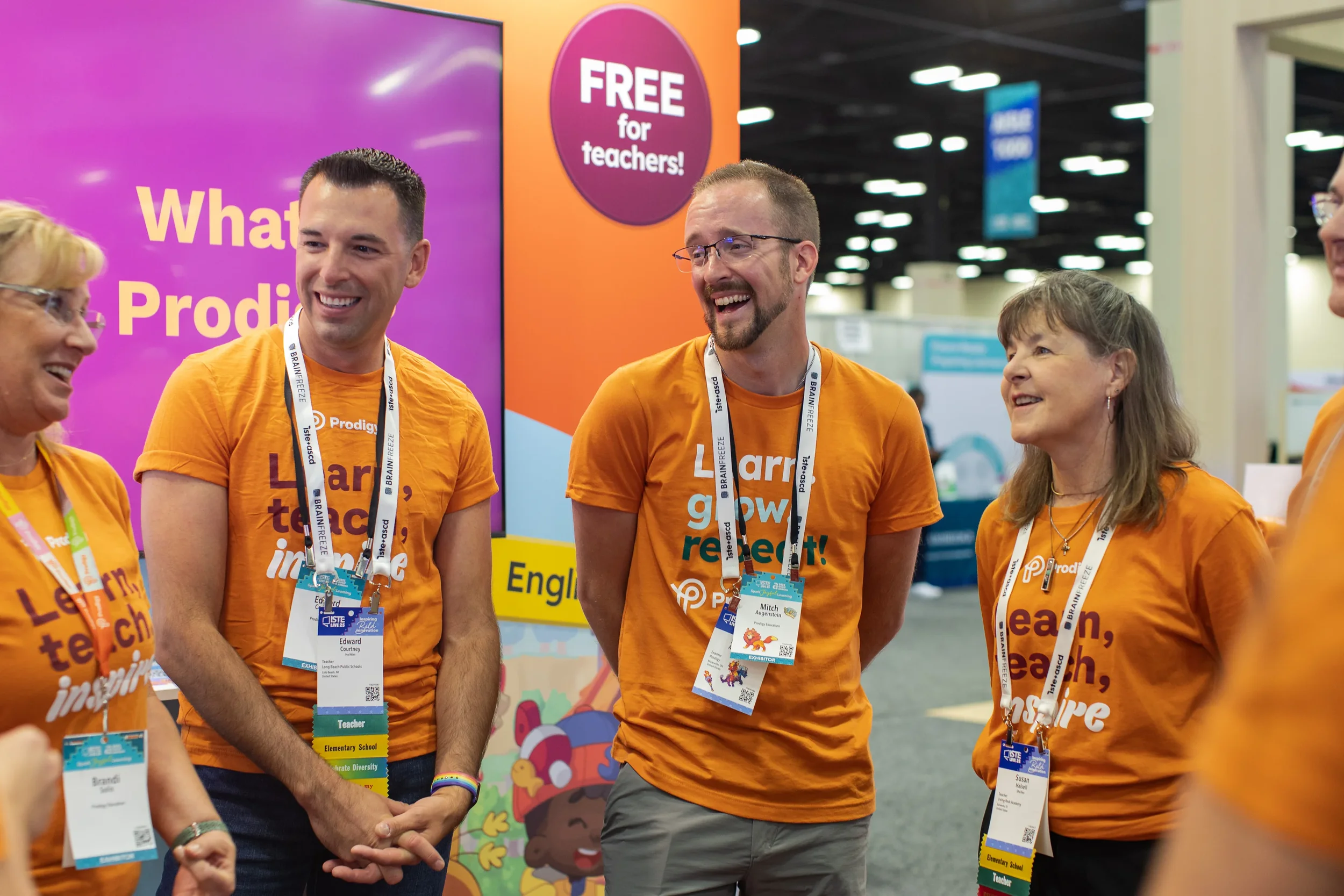 Prodigy team members in branded orange shirts laughing together at the ISTE education technology conference booth.