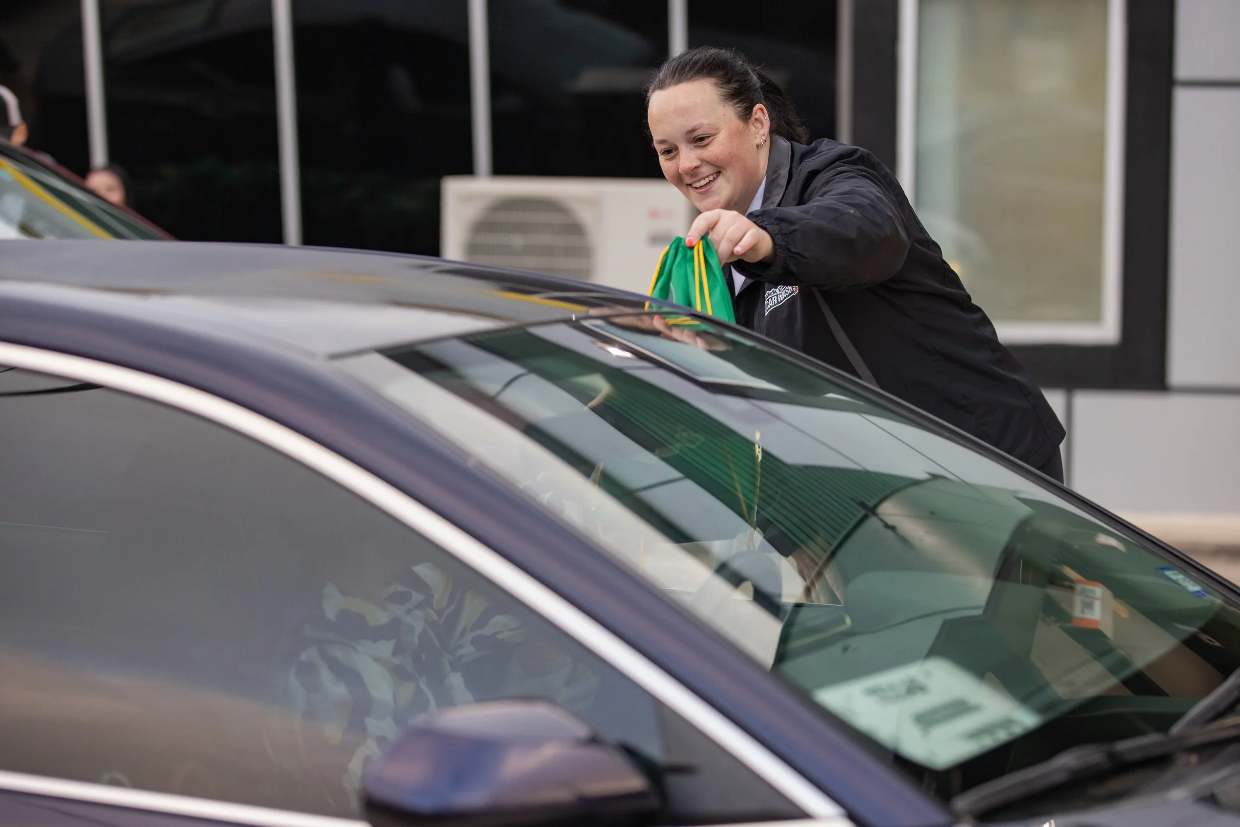 Car wash employee smiling while assisting a customer vehicle with service preparation.