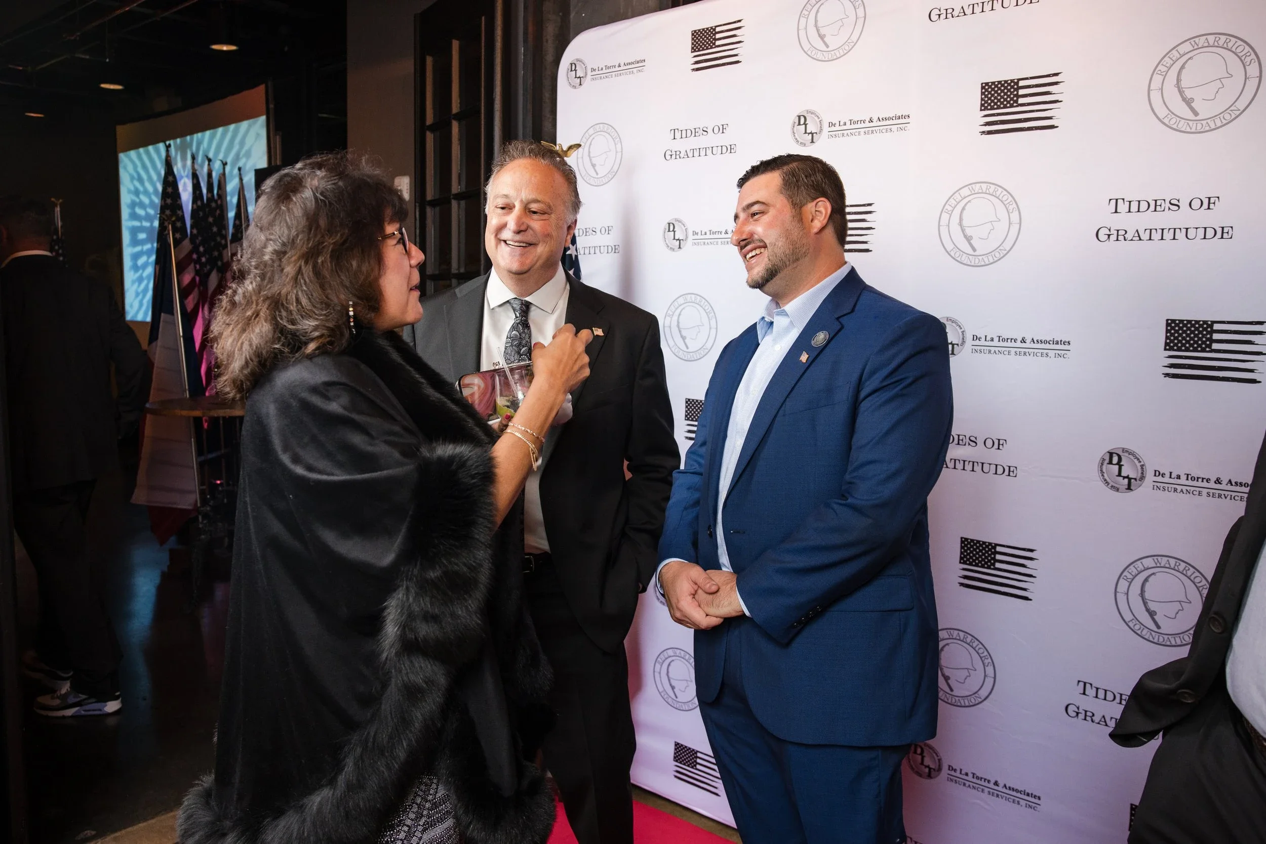 Guests networking on the red carpet at the Tides of Gratitude event in front of branded step-and-repeat backdrop.