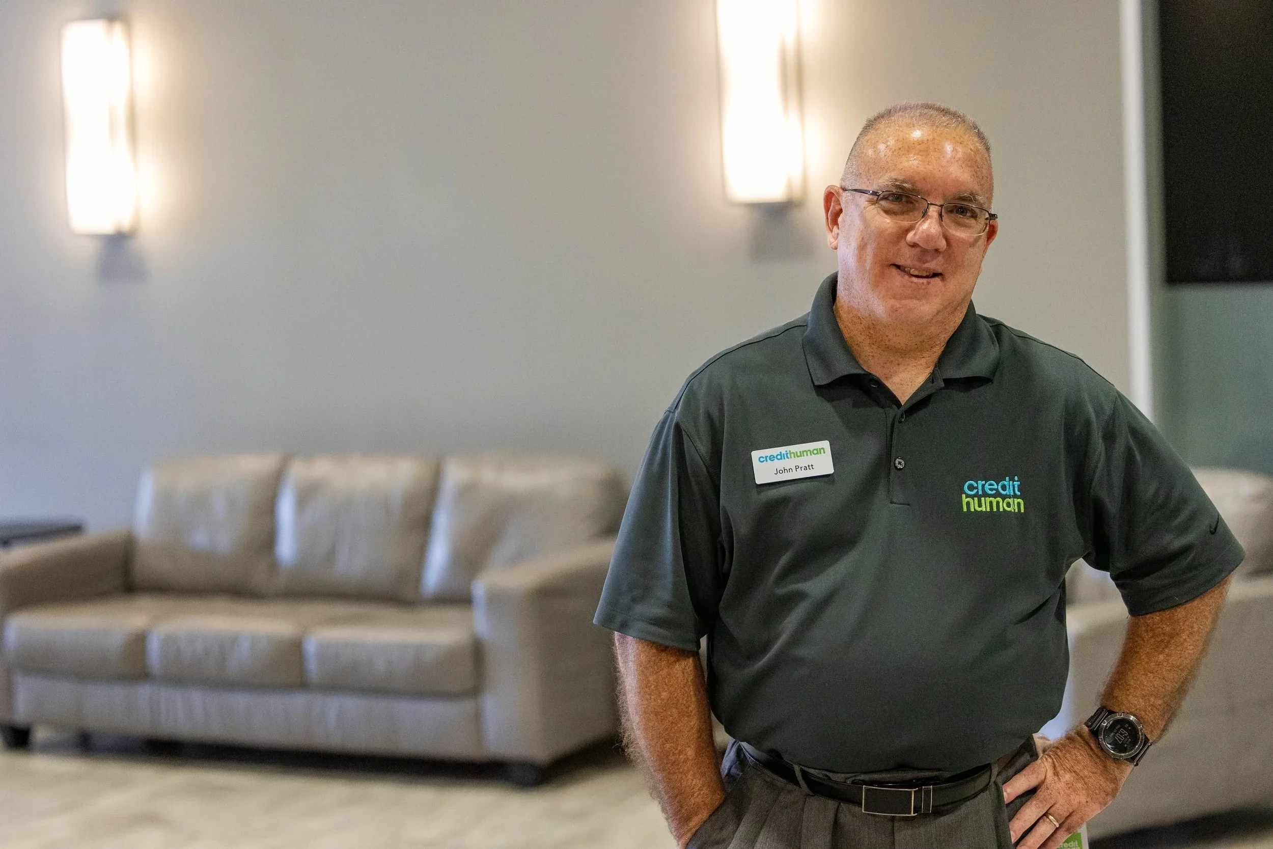 Credit Human employee standing in office lounge wearing branded company polo for corporate portrait.