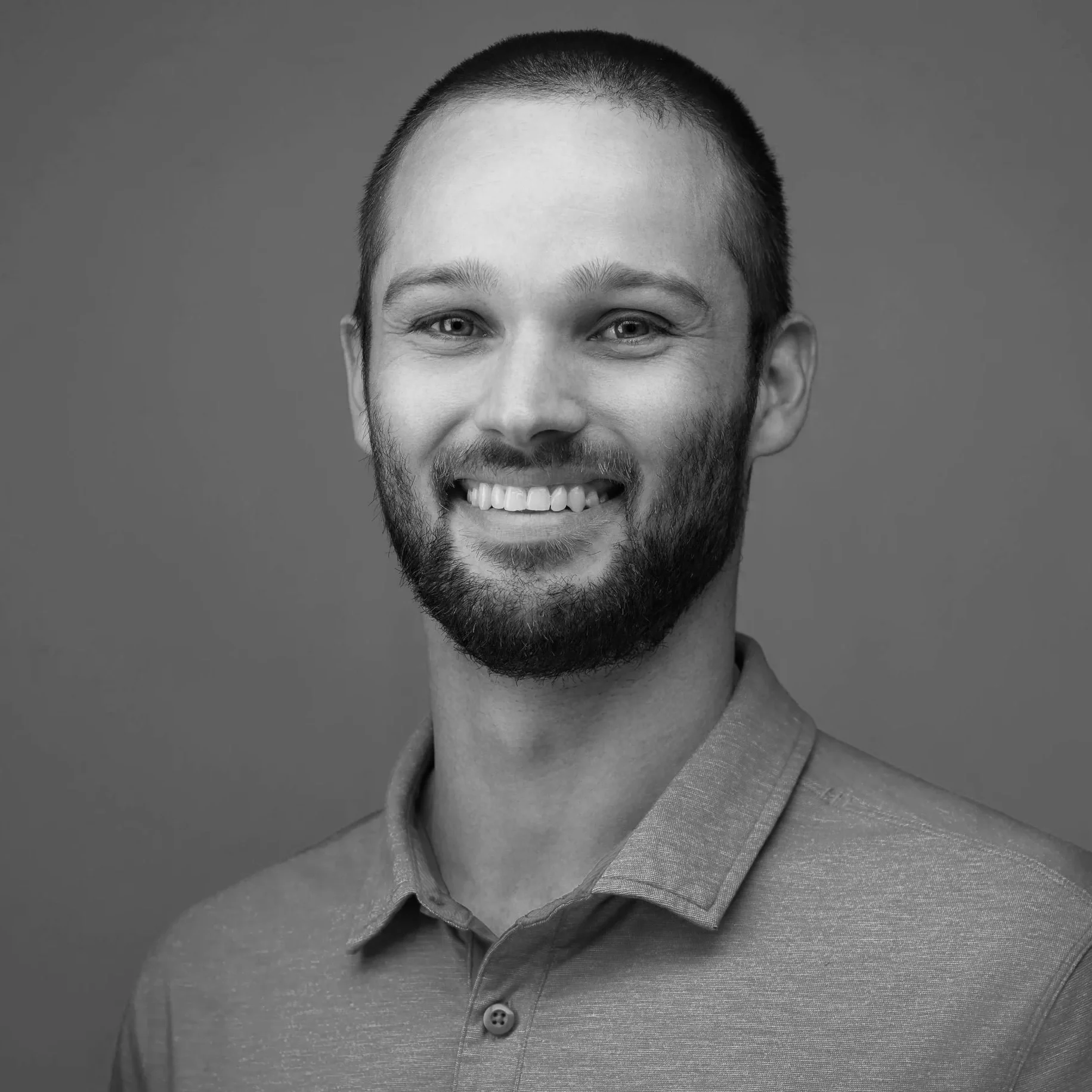 Professional headshot of a smiling man in a blue polo shirt against a neutral gray background, photographed in San Antonio.