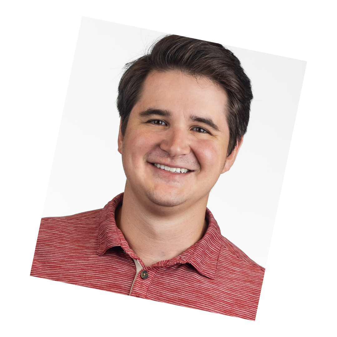 Business headshot of a man in a red collared shirt, smiling in front of a white background.