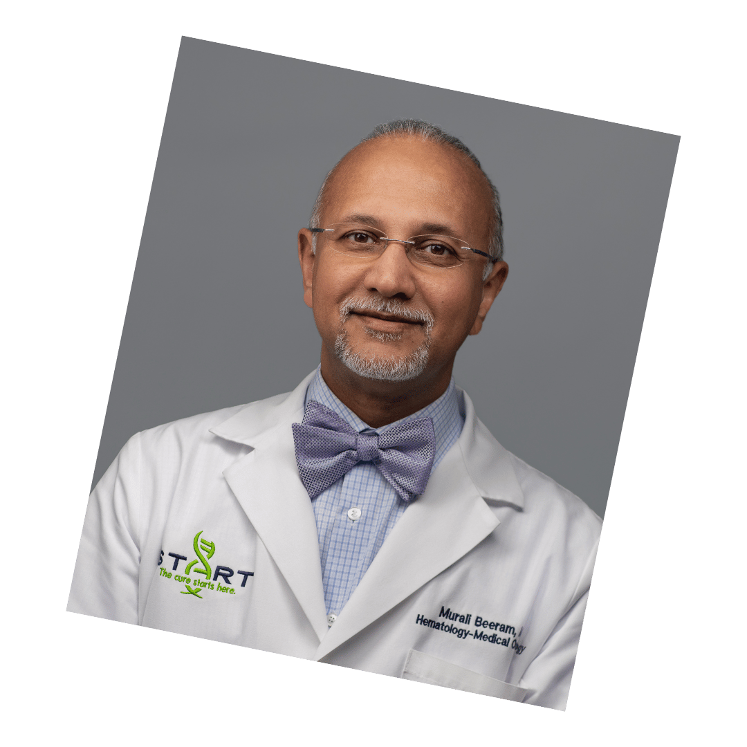 Professional headshot of a male doctor wearing glasses, a bow tie, and a white medical coat, posed against a gray background.