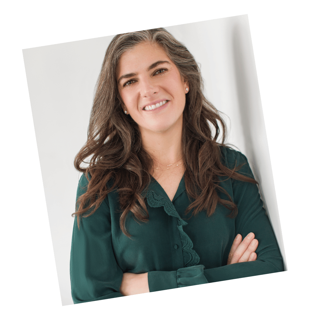 Professional headshot of a woman in a green blouse with long hair, smiling confidently with arms crossed.