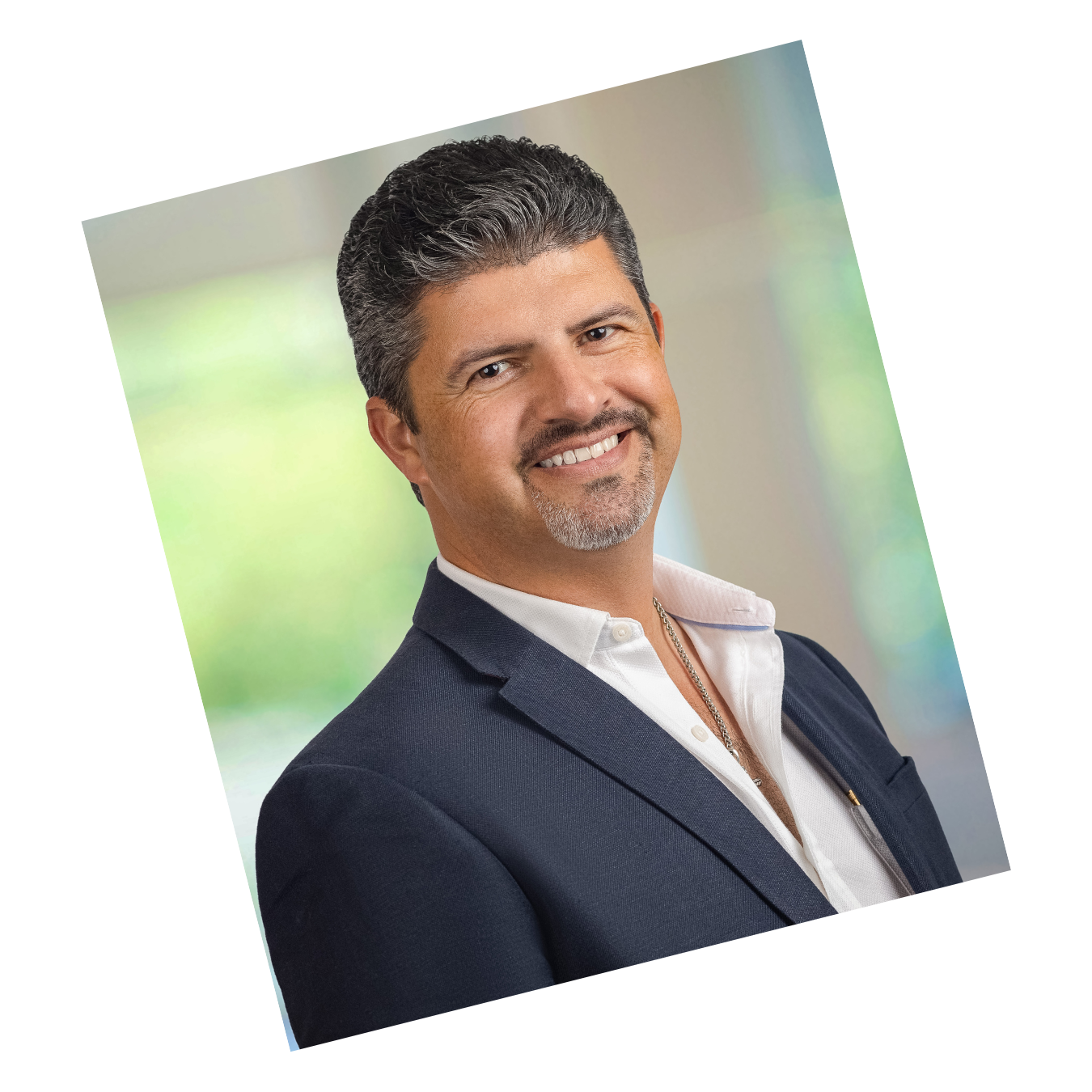 Professional headshot of a man with salt-and-pepper hair and goatee wearing a navy suit, smiling in front of a blurred background.