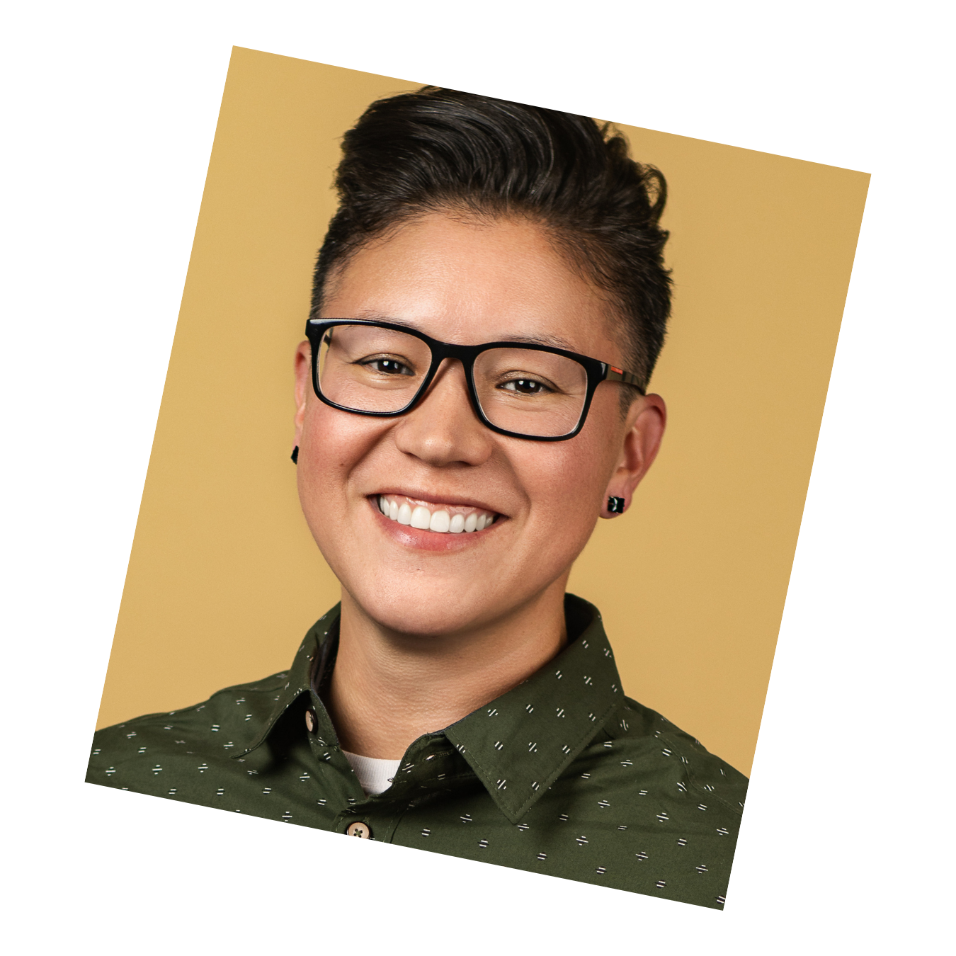 Corporate headshot of a person with short hair, glasses, and green collared shirt smiling against a mustard background.