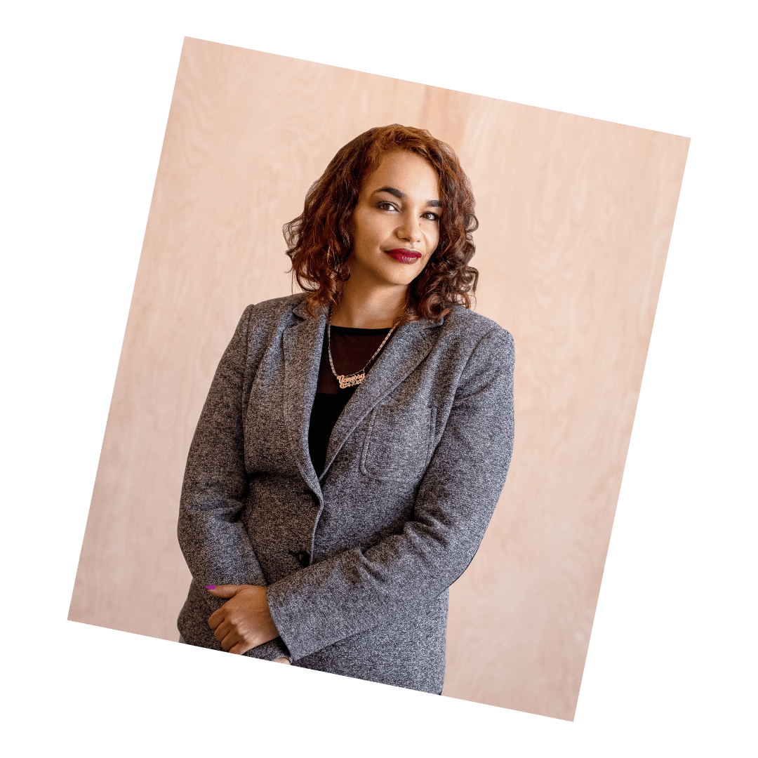 Business headshot of a confident woman in a gray blazer against a warm-toned background, captured by Meet the Bryants Photography.