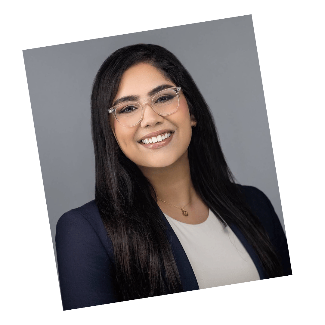 Modern professional headshot of a smiling woman wearing glasses and a dark blazer, photographed against a gray backdrop.