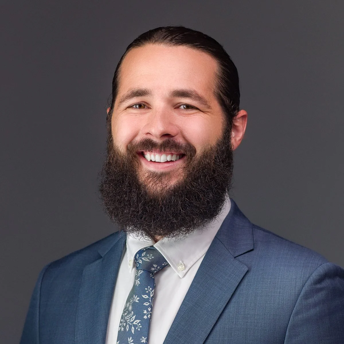 Professional headshot of a man with a full beard wearing a blue suit and floral tie, captured by Meet the Bryants Photography in San Antonio, Texas.