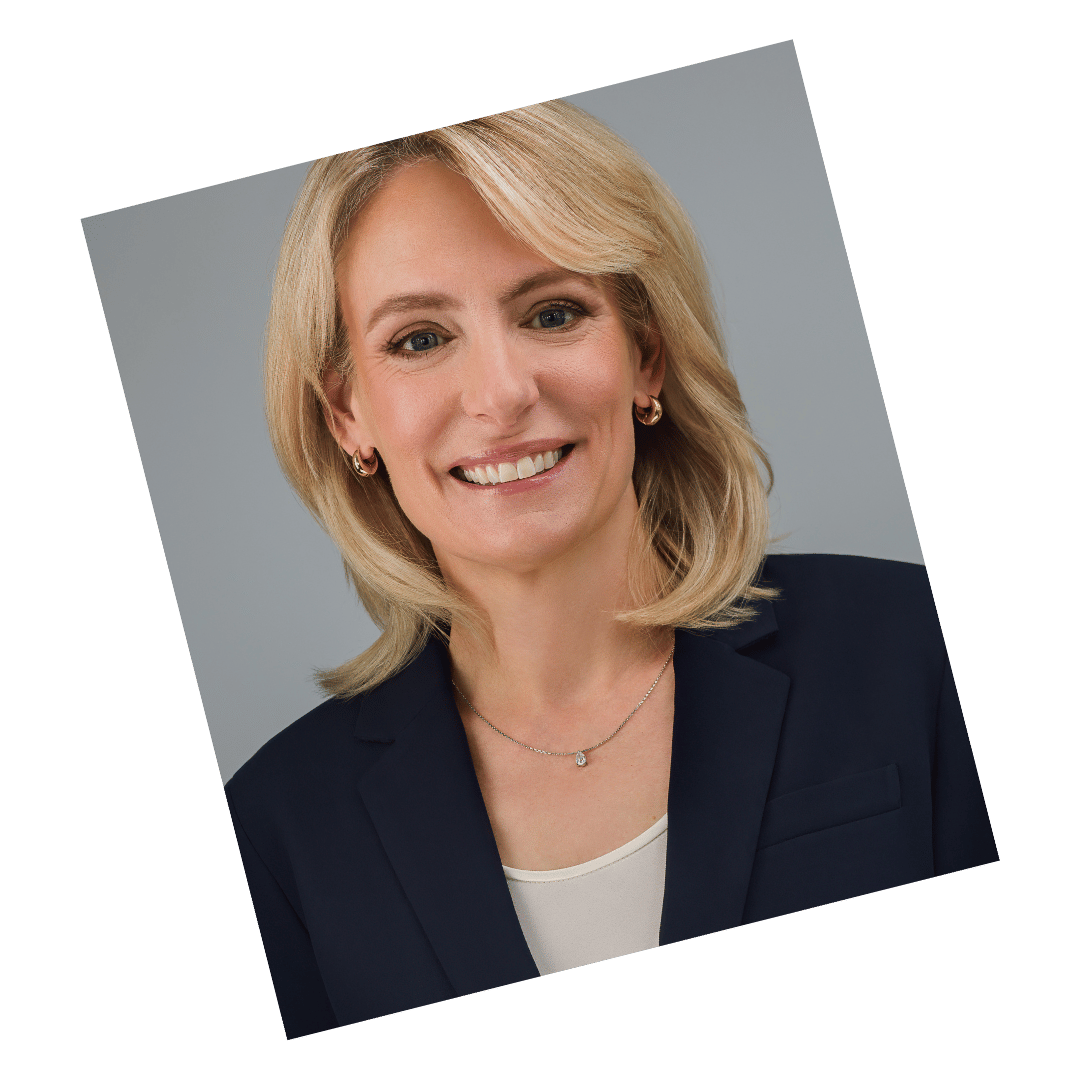 Executive headshot of a woman in a navy blazer and cream blouse, standing confidently against a neutral gray background, photographed by Meet the Bryants Photography.