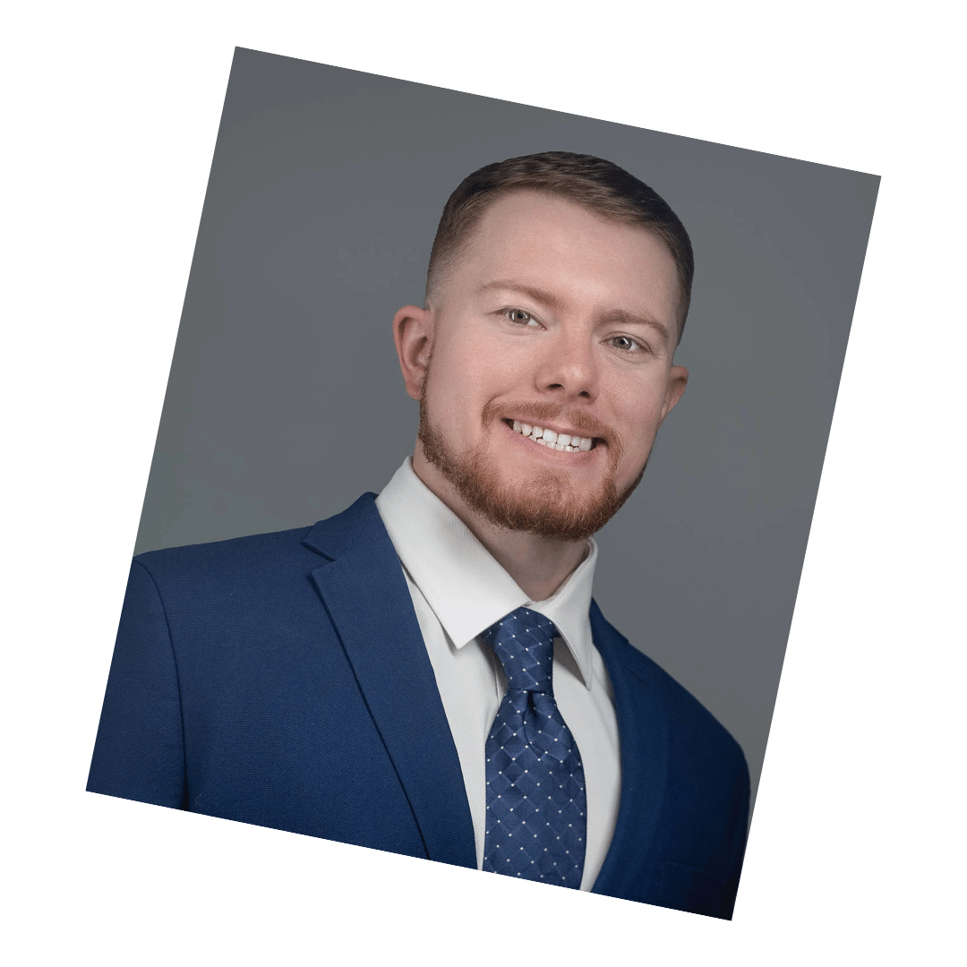 Professional corporate headshot of a man in a navy blue suit and tie against a neutral gray background, photographed by Meet the Bryants Photography in San Antonio, Texas.