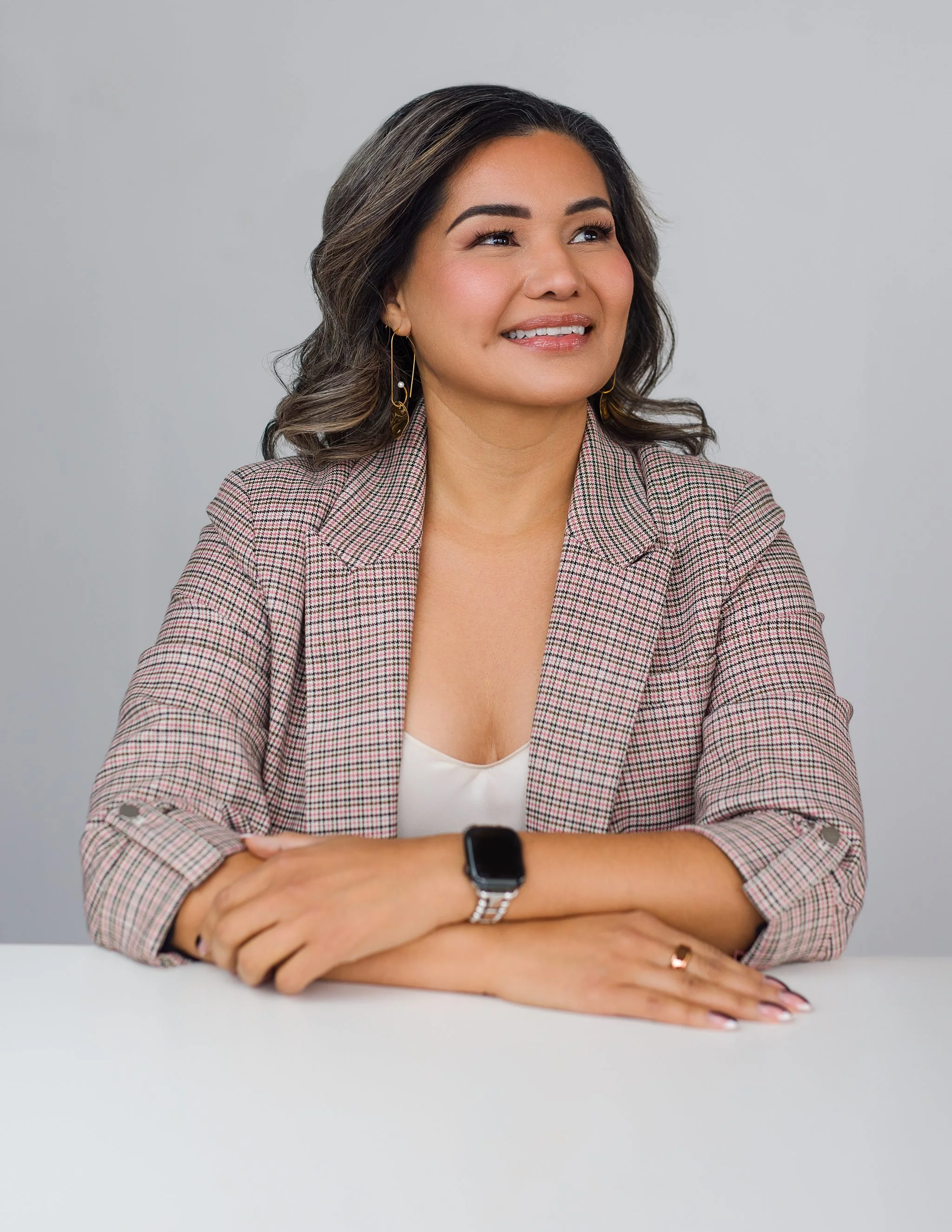 Professional headshot of a woman in a pink checkered blazer smiling while seated at a desk, San Antonio corporate photography.