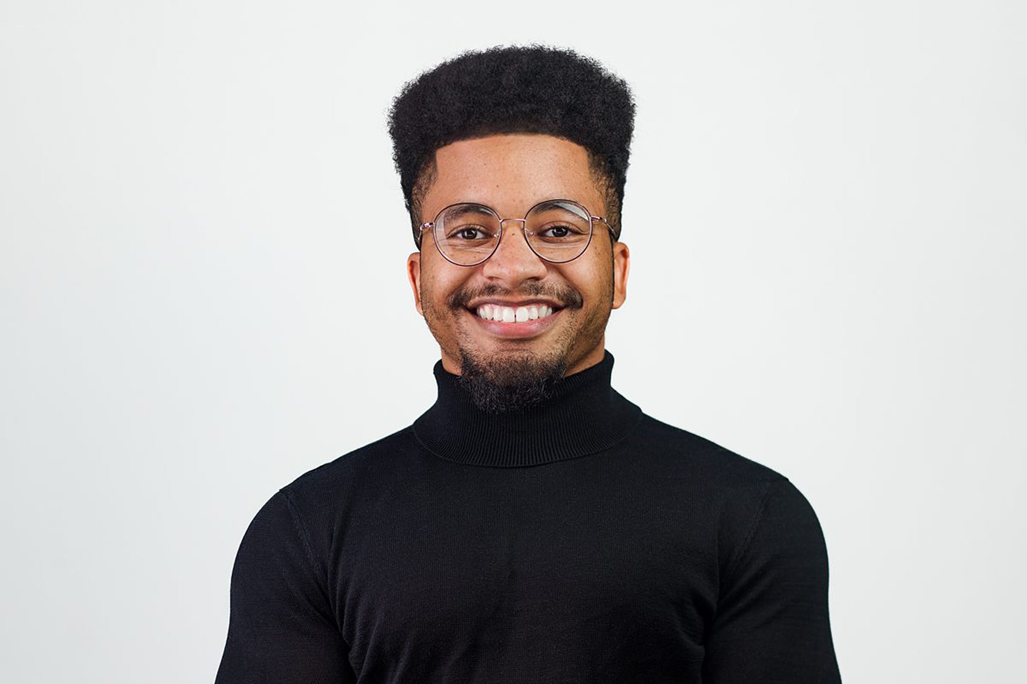 Corporate headshot of a young man in glasses wearing a black turtleneck and smiling confidently, San Antonio headshot session.