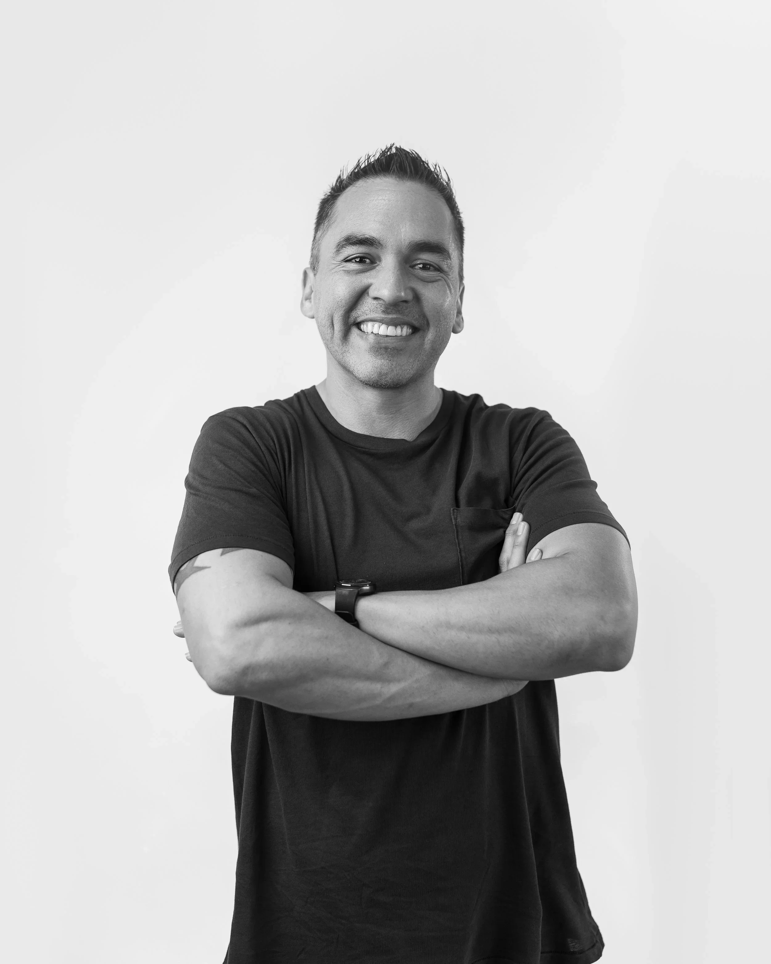 Black and white modern headshot of a man in a casual t-shirt with arms crossed, smiling confidently.