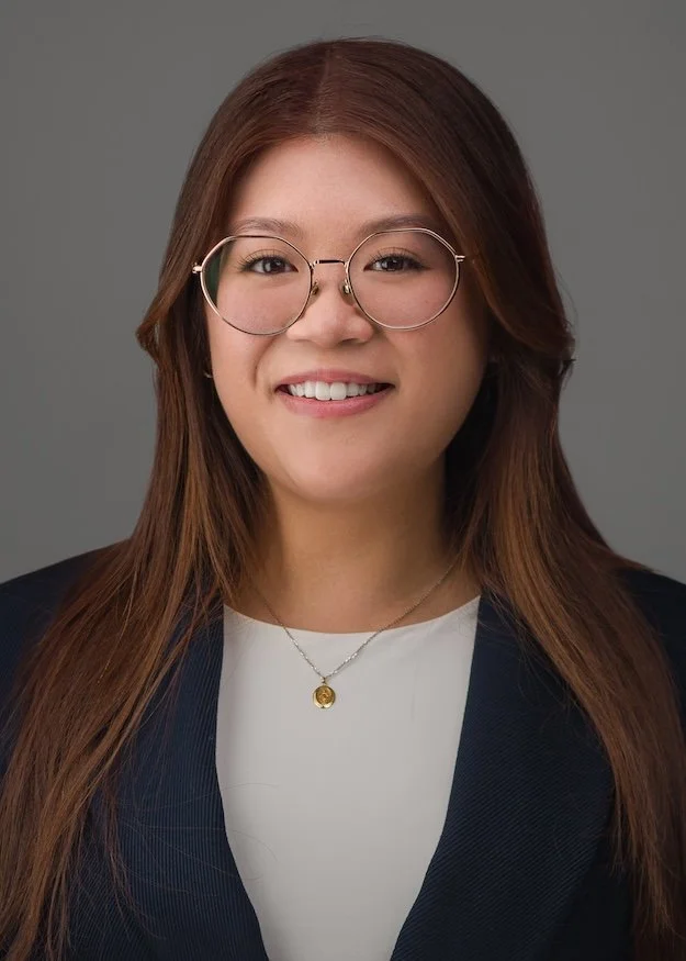 Residency headshot of a woman wearing glasses and a navy blazer over a white blouse, photographed on a gray backdrop by Meet the Bryants Photography.