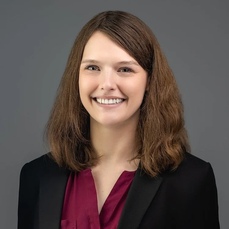 Professional headshot of a woman wearing a burgundy blouse and black blazer, captured against a soft gray background by Meet the Bryants Photography in San Antonio.