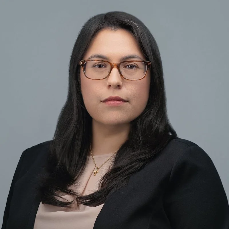 Corporate headshot of a woman with long dark hair wearing glasses and a black blazer, photographed on a soft gray background by Meet the Bryants Photography.