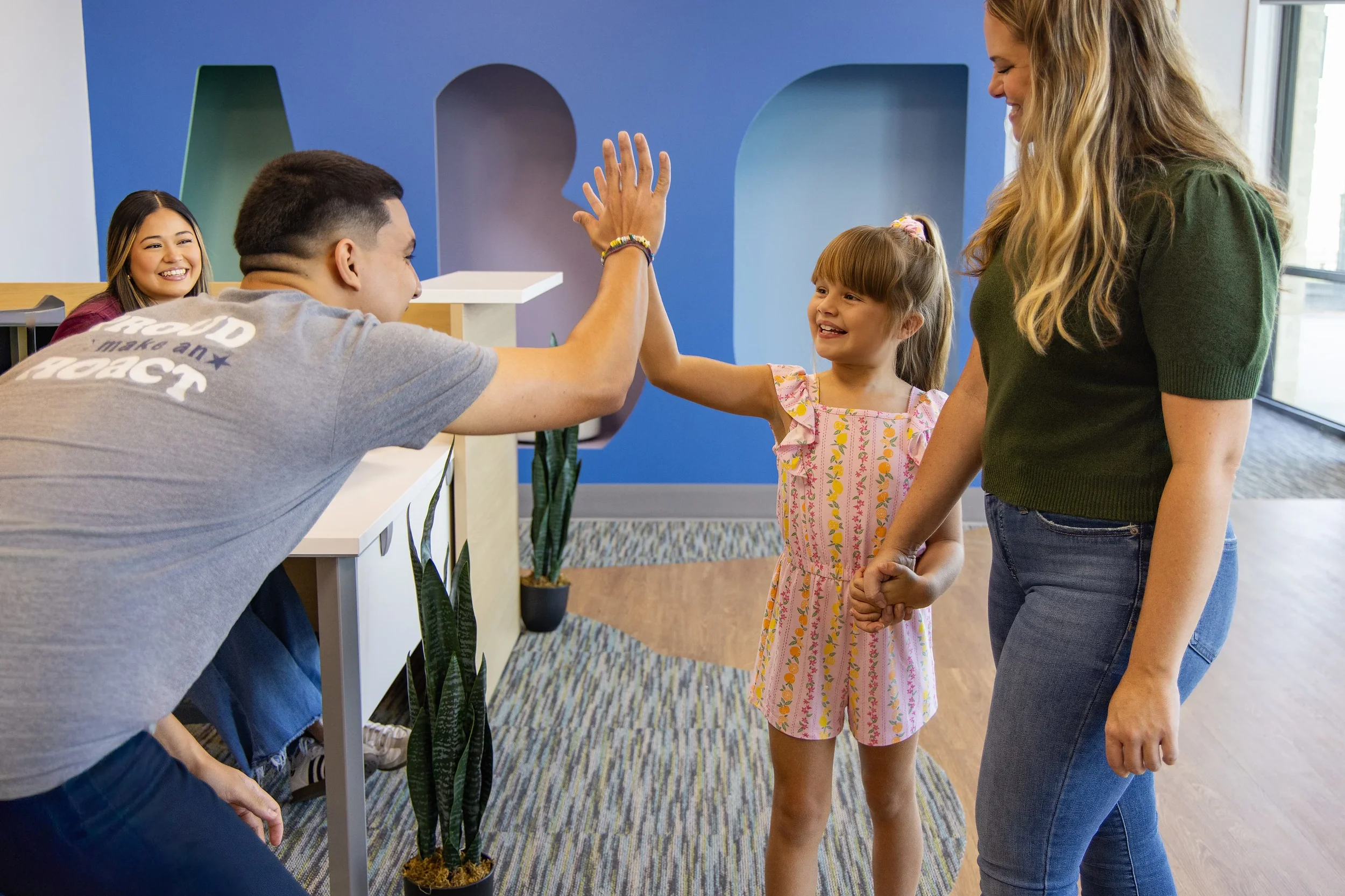 Therapist high-fiving a young girl in the reception area of Action Behavior Centers San Antonio, representing encouragement and community connection.