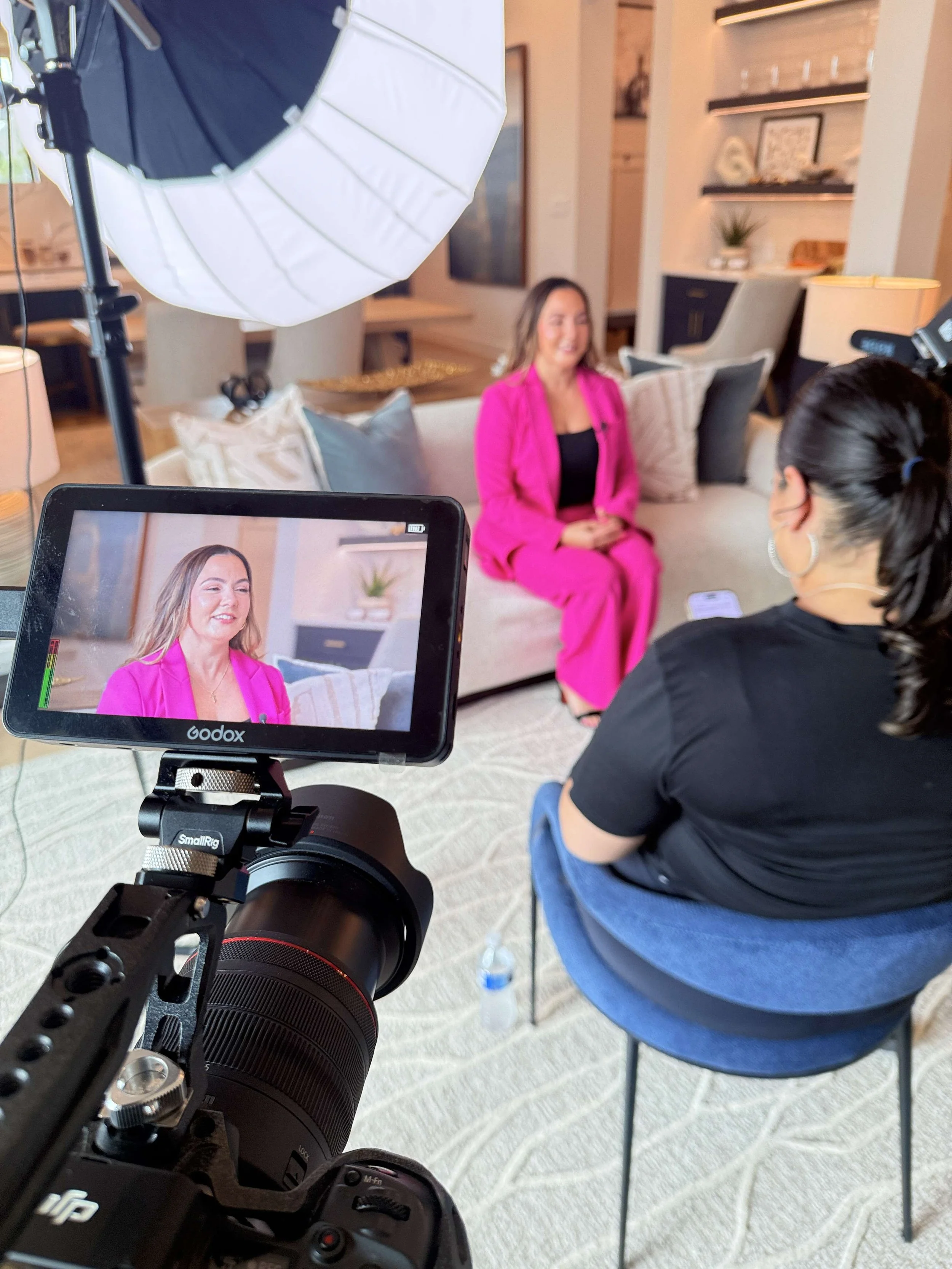 Behind-the-scenes video interview shoot with woman in pink blazer, Godox monitor in foreground, styled living room — Meet the Bryants Photography San Antonio
