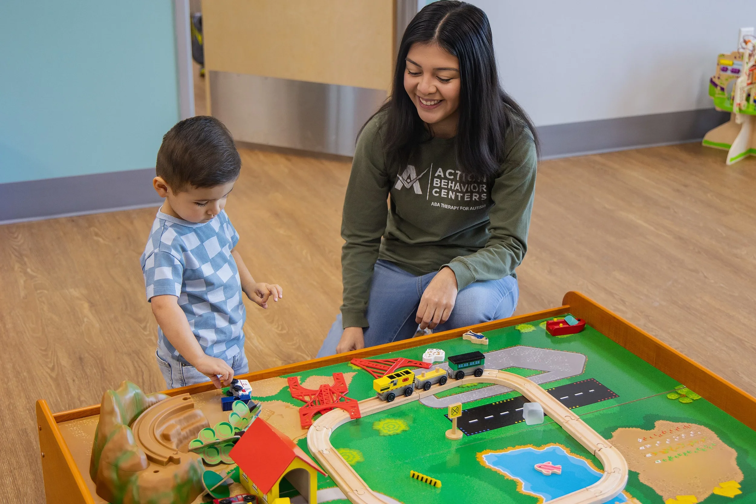 Child and therapist playing with a wooden train set during developmental therapy at Action Behavior Centers in San Antonio, promoting engagement and learning through play.