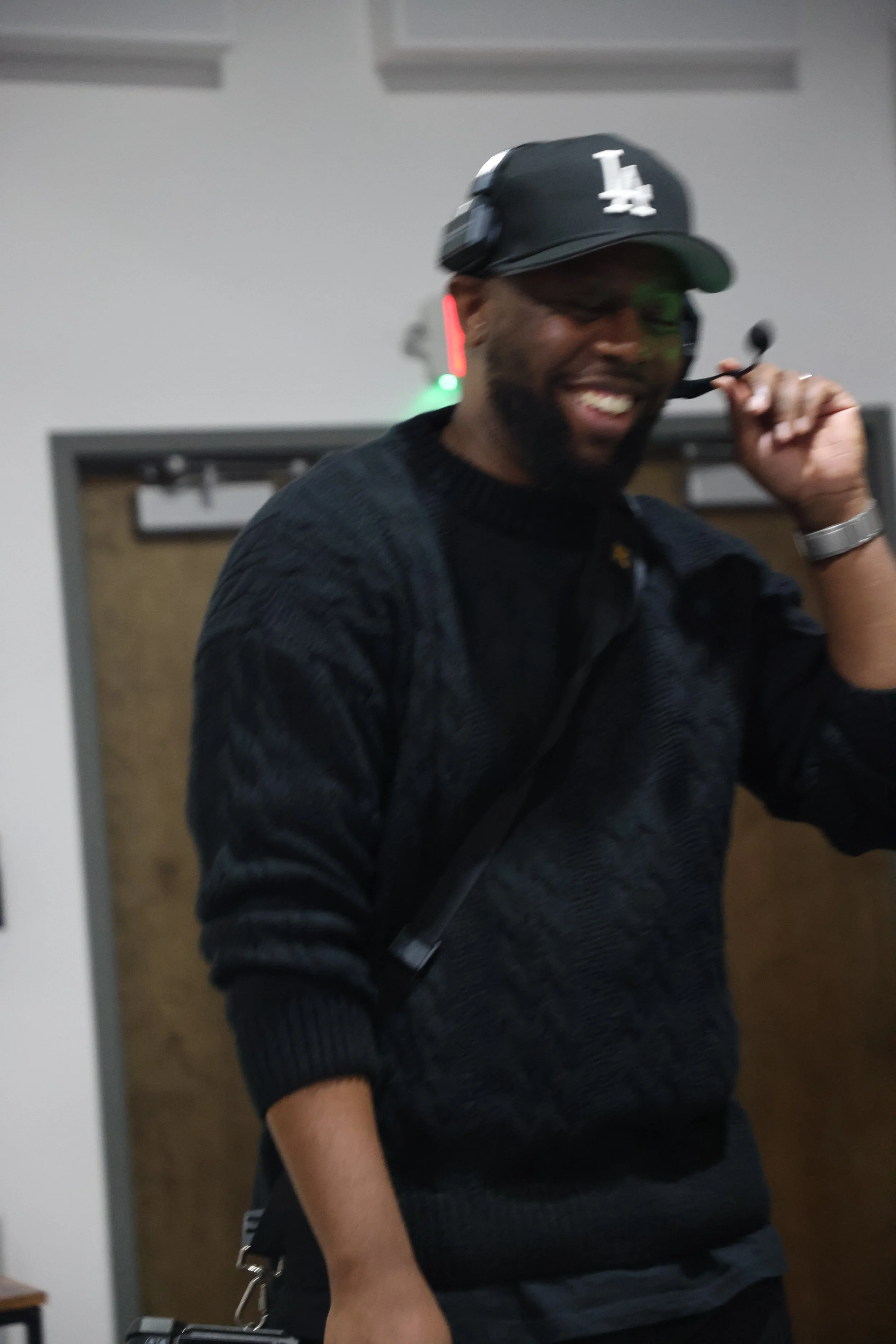 Live event producer wearing a headset and LA cap smiling while coordinating production during an indoor event.